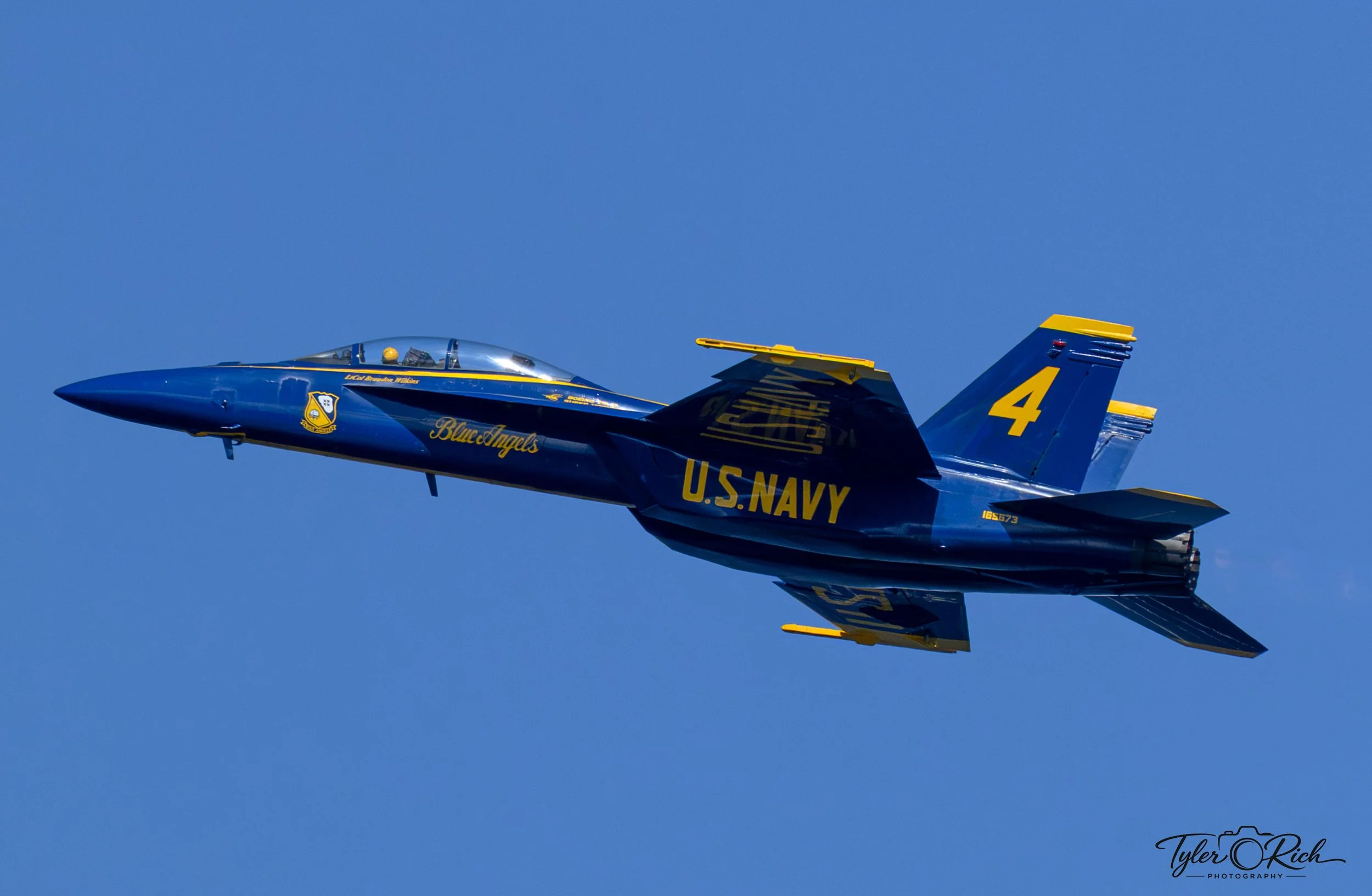 A blue and yellow U.S. Navy fighter jet flying in clear blue sky.