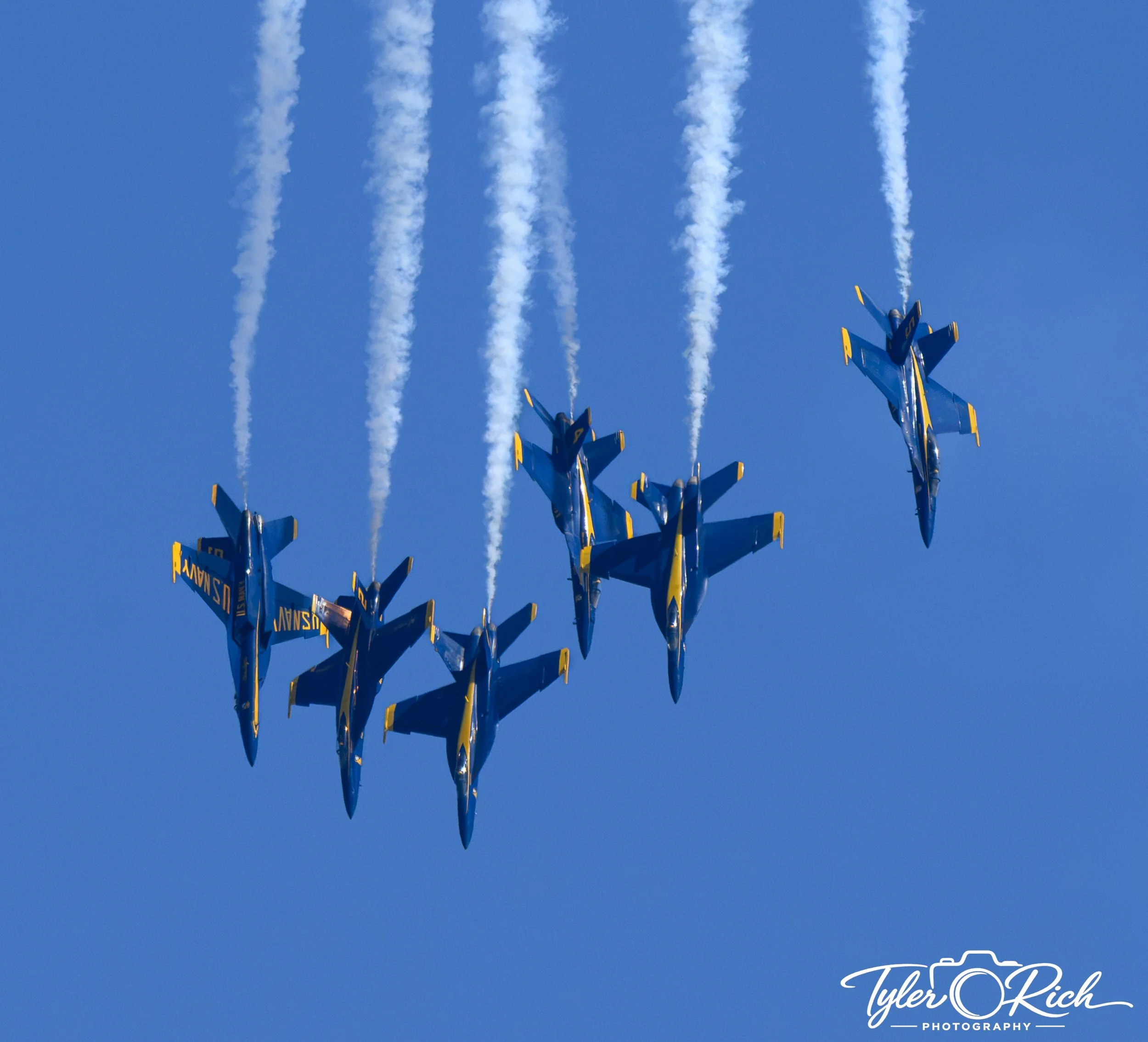 Three jets flying in formation against a blue sky, leaving white smoke trails behind them.