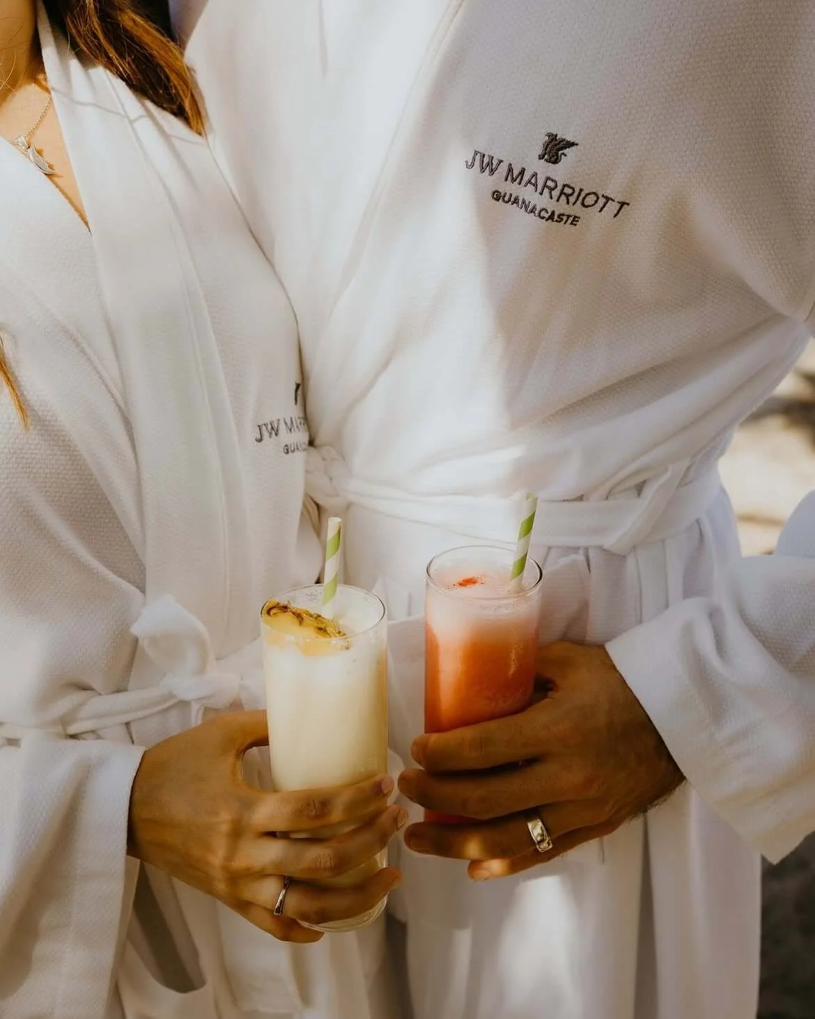 Two people in white robes holding colorful drinks with straws, at JW Marriott Guanacaste.