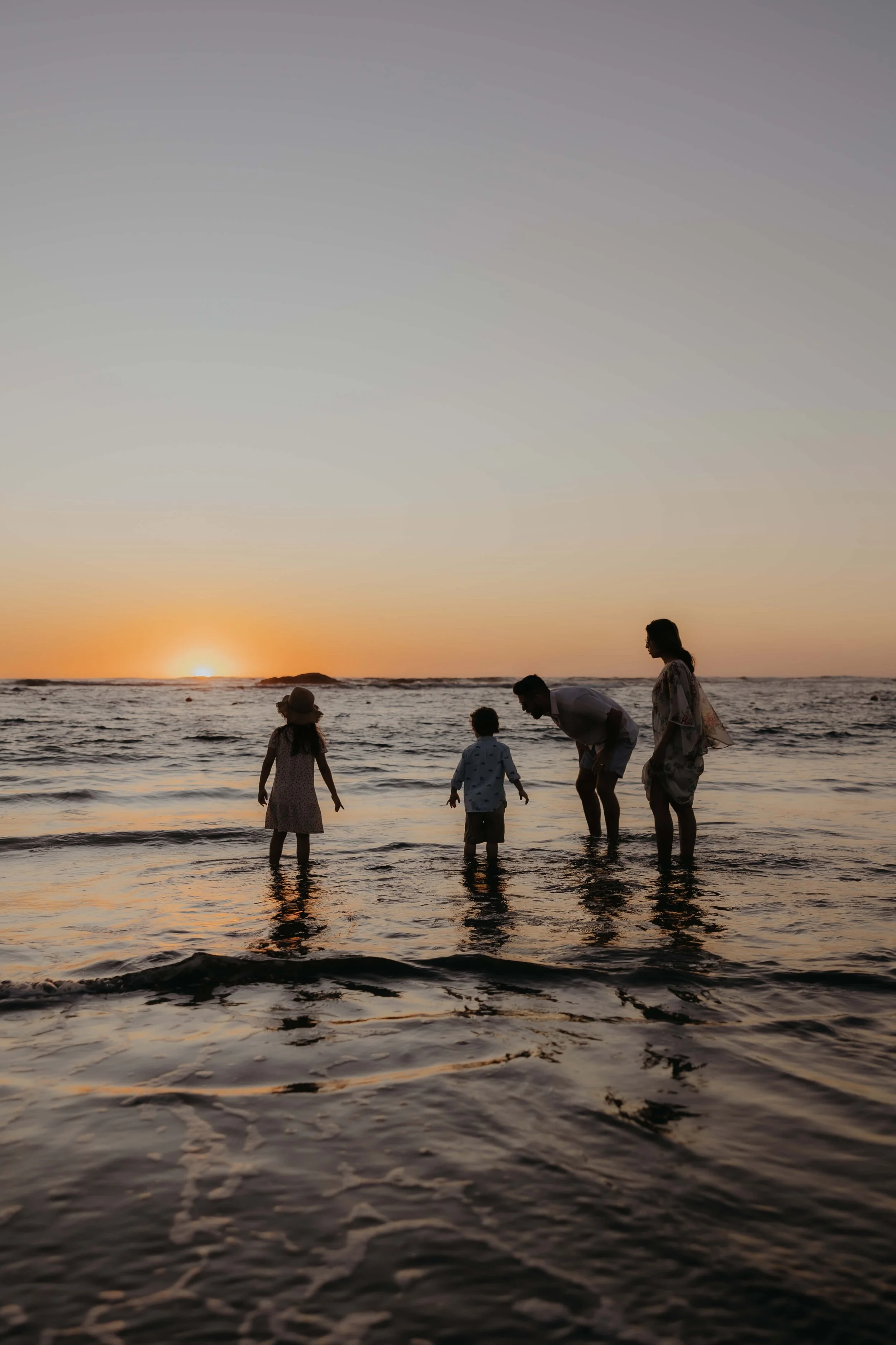 Family of five enjoying a sunset at the beach, playing in the shallow waters.