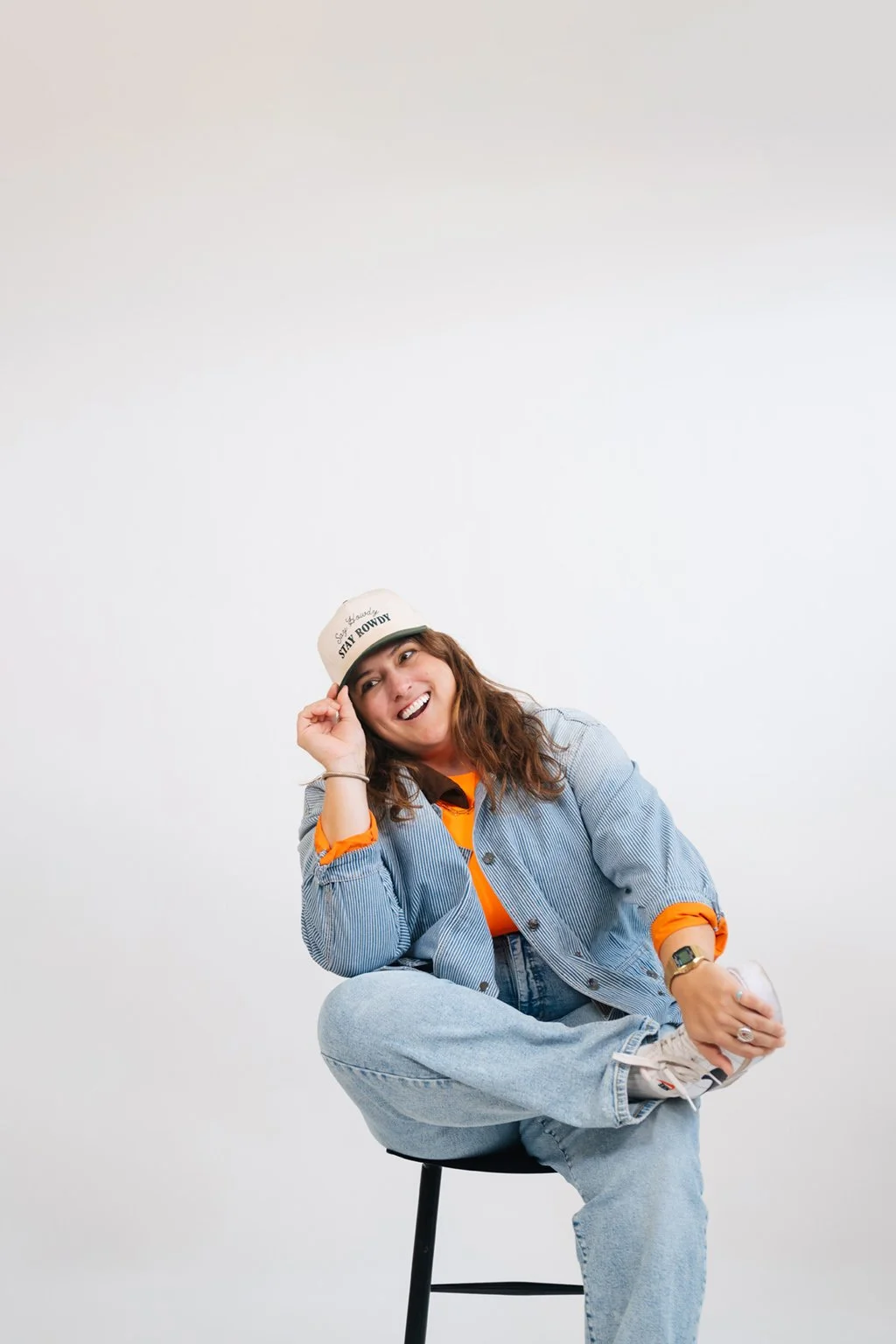 A woman laughing, looking to the side while holding her baseball cap brim.