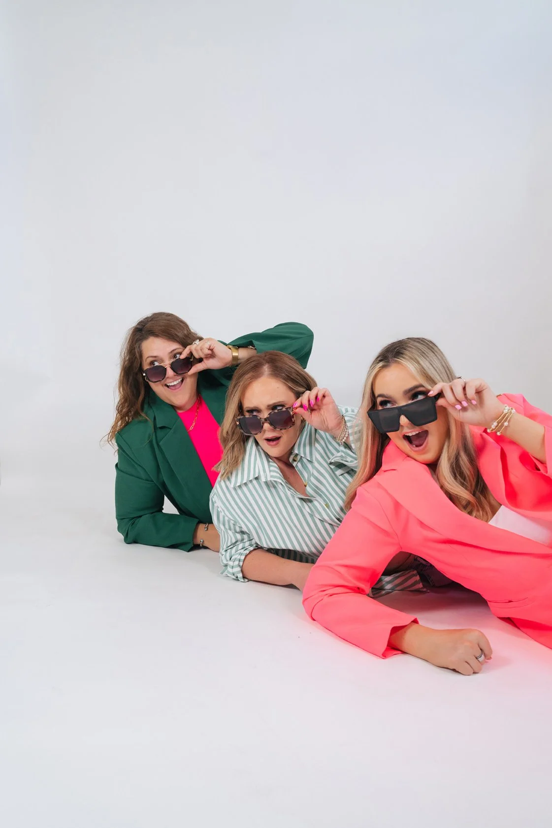 Three members of the Birch & Bloom team lying on the floor in colorful blazers, peeking over their sunglasses