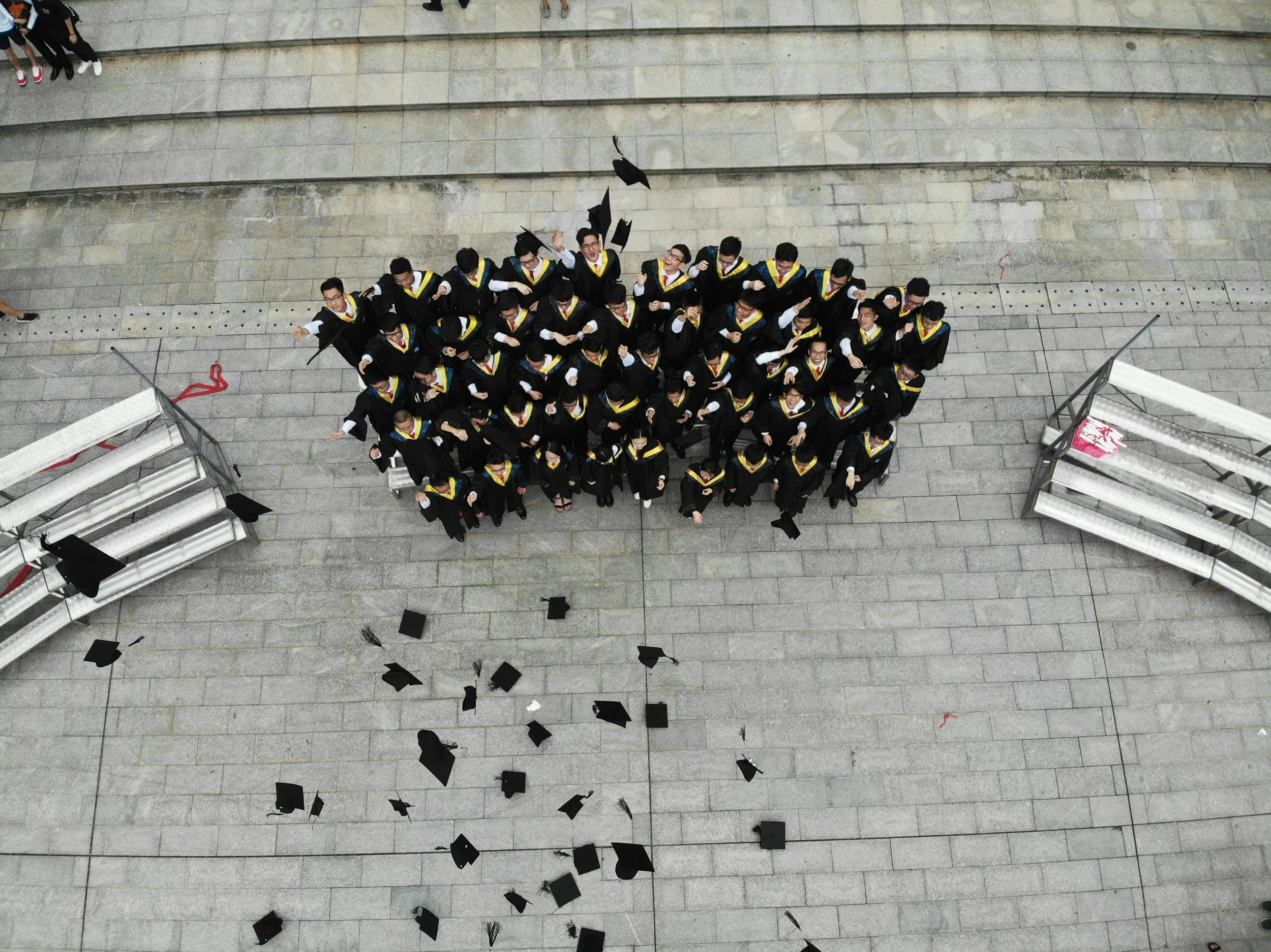 Aerial view of a group of graduates in caps and gowns celebrating on stairs at a graduation ceremony.
