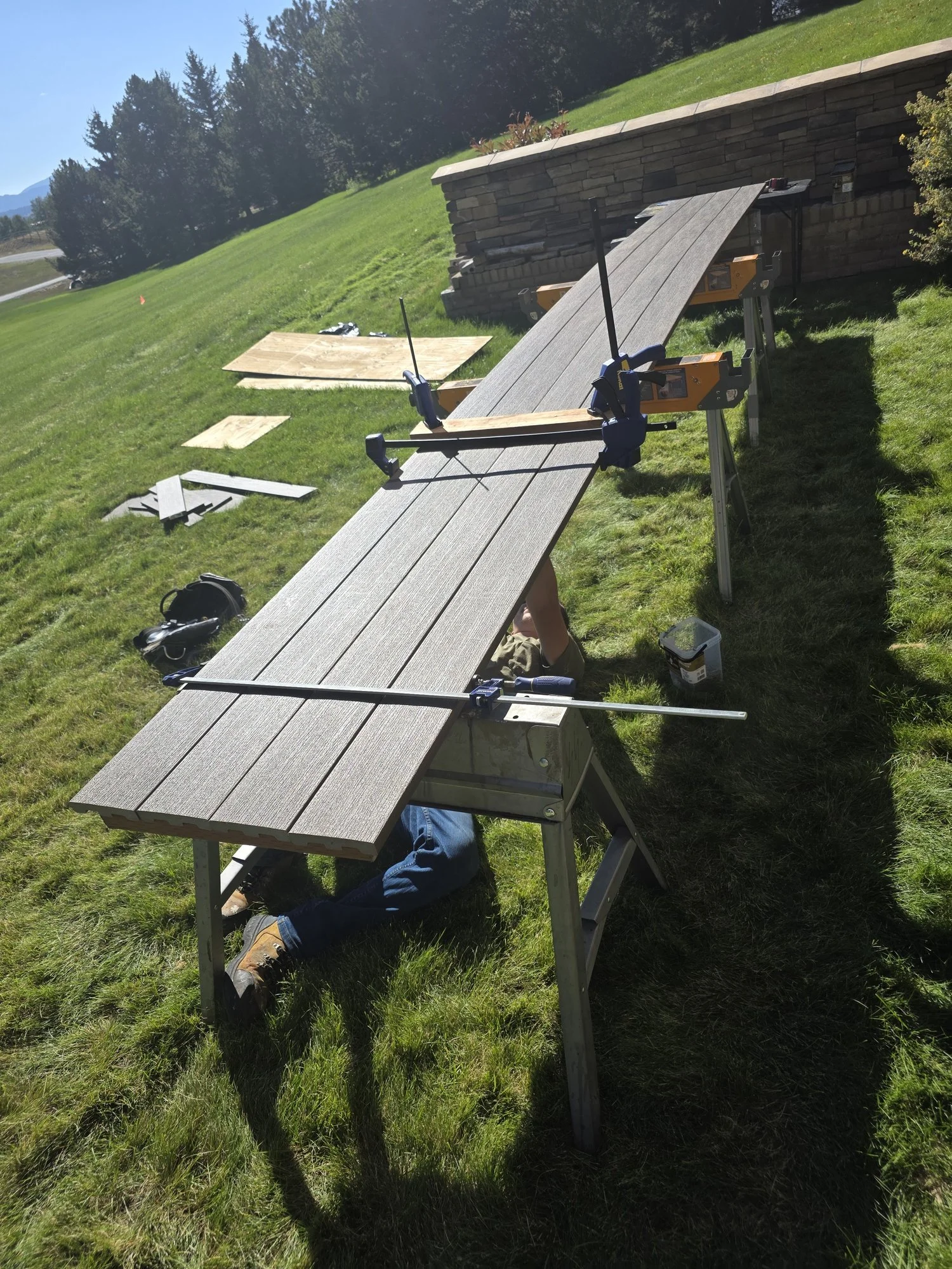 Composite decking boards glued and clamped on sawhorses before being set on the planter wall