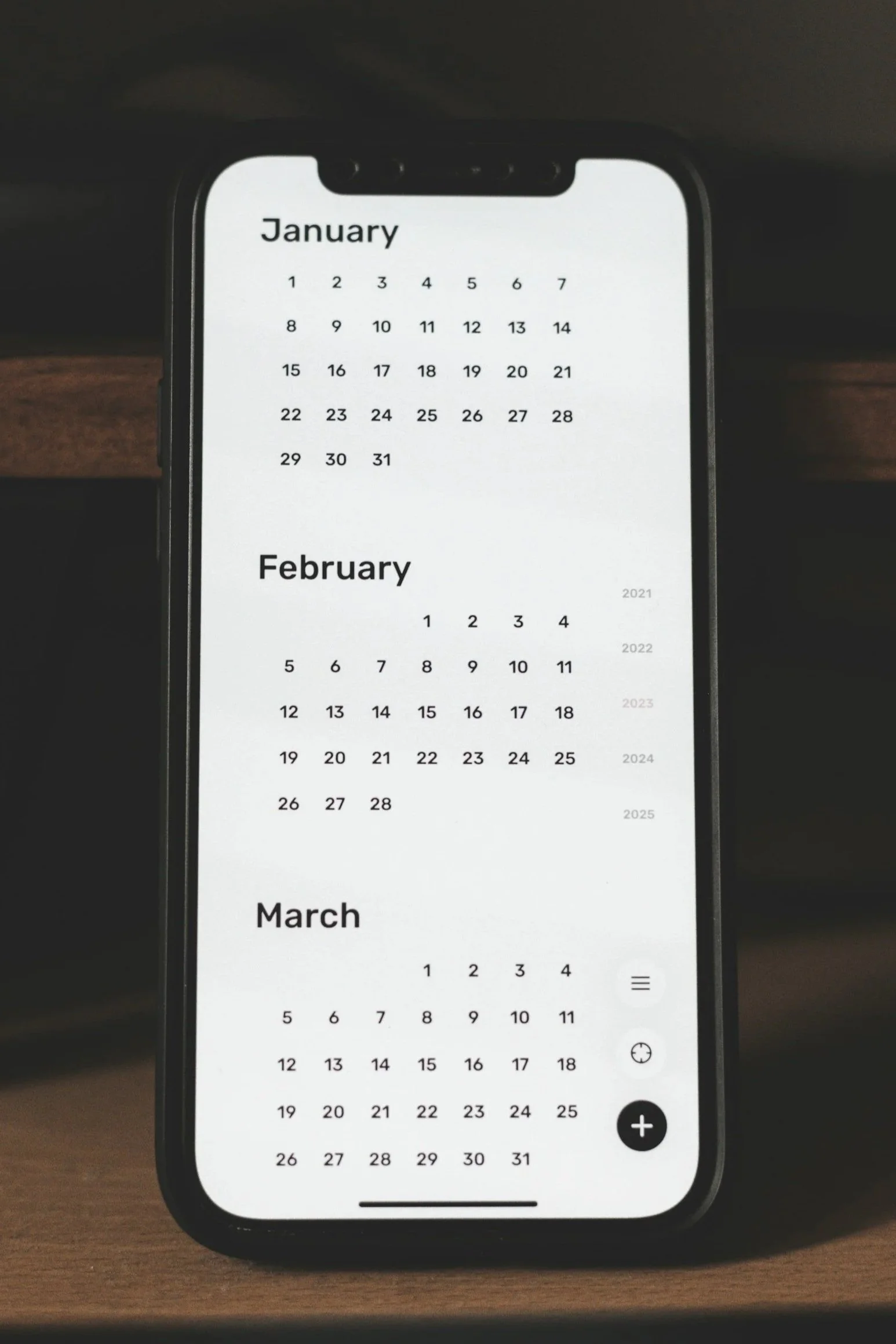 A top-down, close-up photograph of a smartphone displaying a minimalist calendar app layout on its screen. The interface features clean typography showing the months of January, February, and March with their respective numeric dates