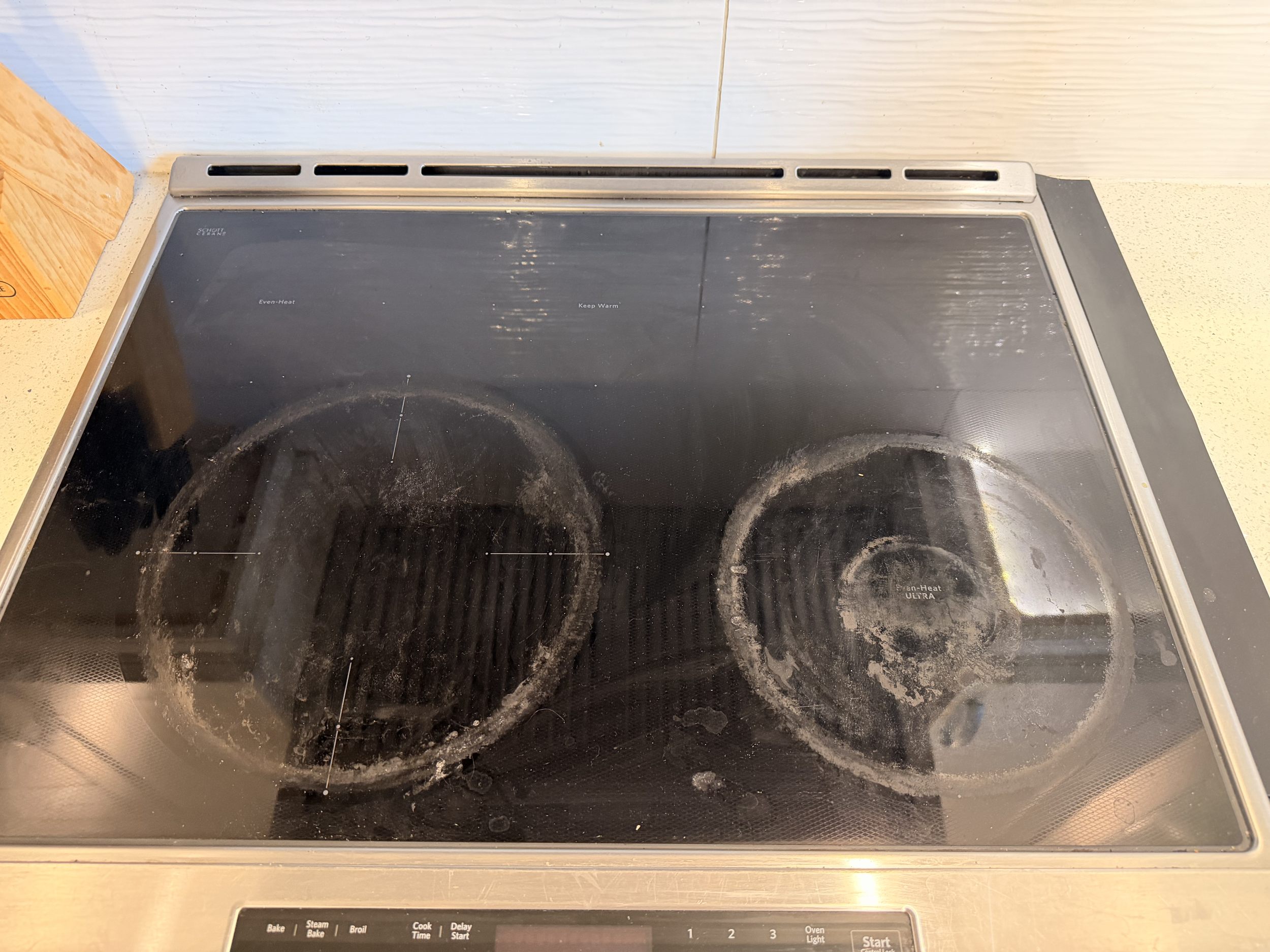 A black electric stovetop with four burners and a digital control panel at the front, showing signs of use and dirt around the burners.