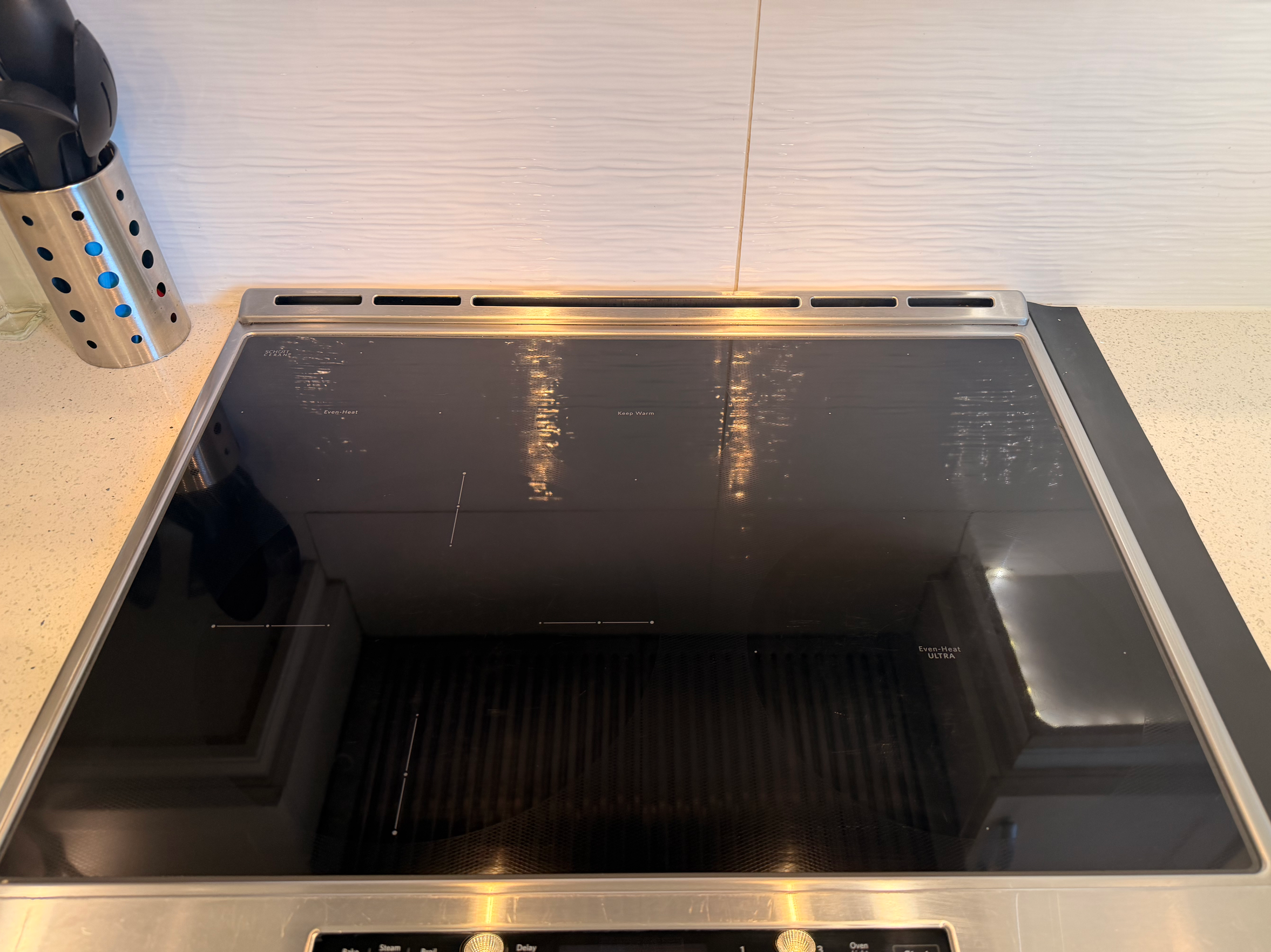 A modern induction stovetop with black glass surface, control knobs, and a metal utensil holder with spoons on the kitchen counter.