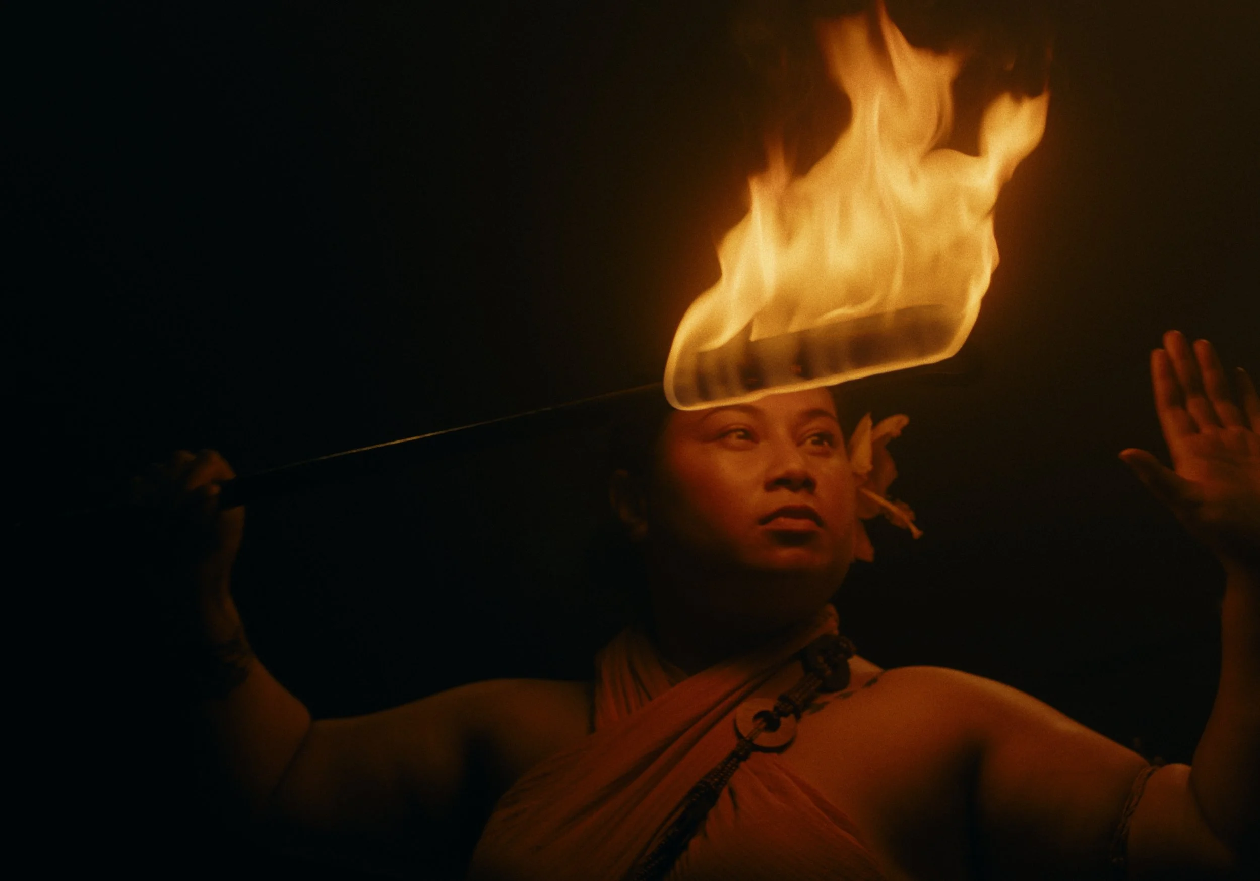 Person holding a glass surface with fire on it, glasses on her head, and night sky in the background.