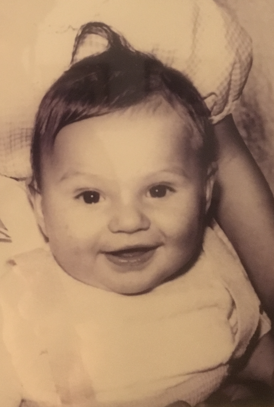 Black and white photo of a smiling baby with short, dark hair, wearing a light-colored outfit.