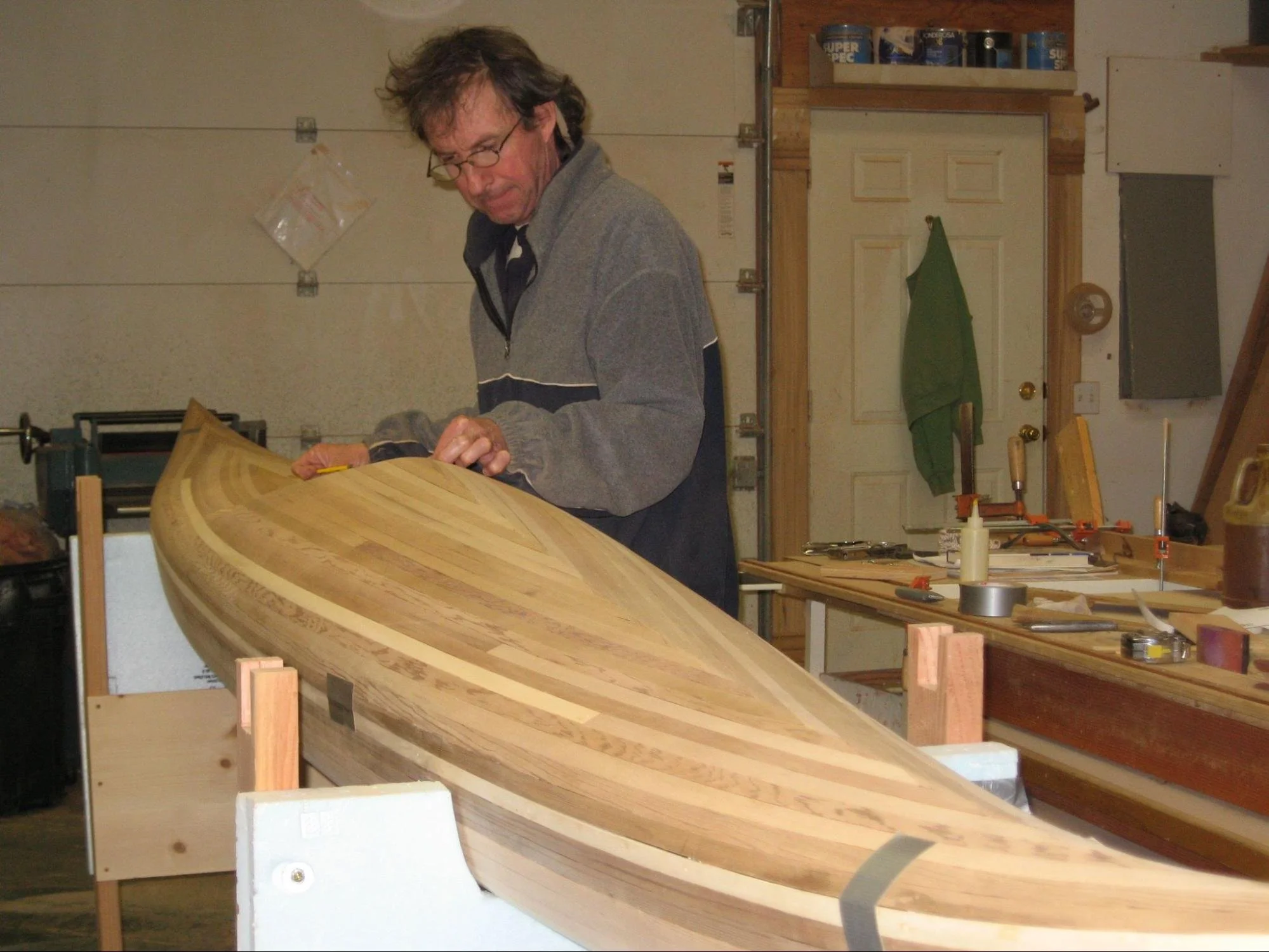 A man working on a wooden boat in a workshop, surrounded by tools and materials.