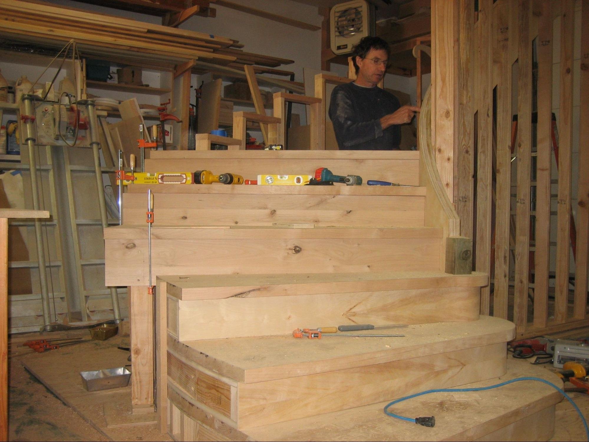 A man working on a woodworking project in a workshop filled with tools and wooden materials.