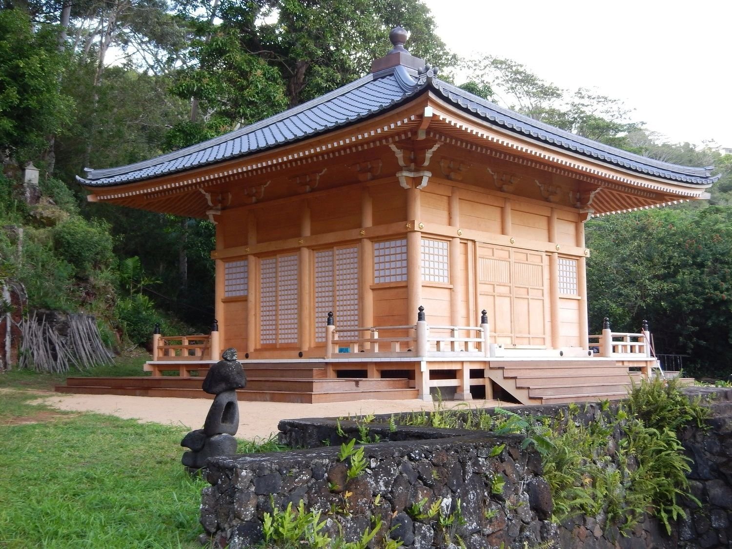 Traditional Japanese wooden shrine with a dark tiled roof, set outdoors among greenery and trees.