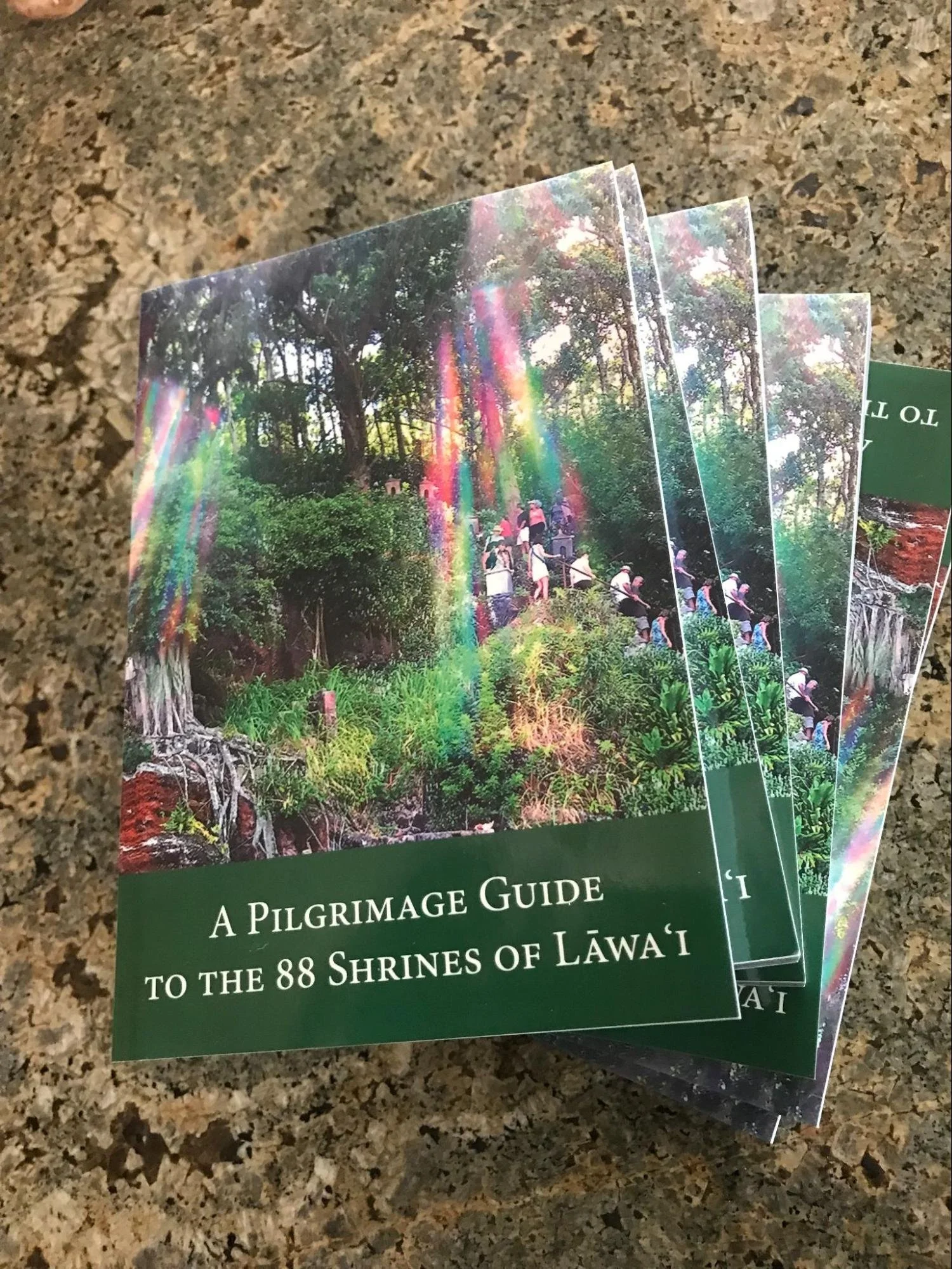 A pamphlet with a forest scene and a rainbow light effect on the cover, titled 'A Pilgrimage Guide to the 88 Shrines of Lāʻwai'.