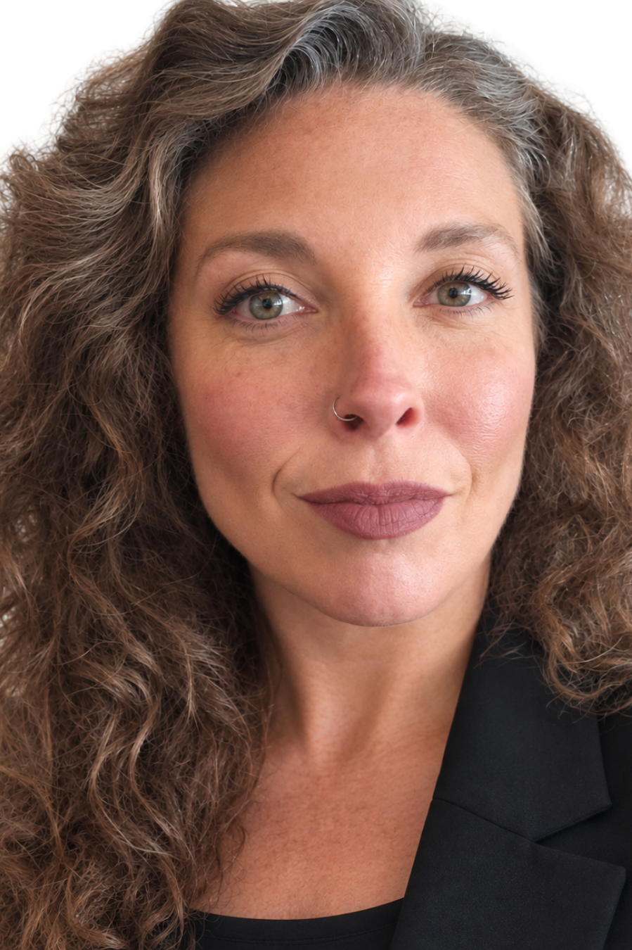 Close-up of a woman with curly brown hair, light skin, gray eyes, and a nose ring wearing a black blazer.