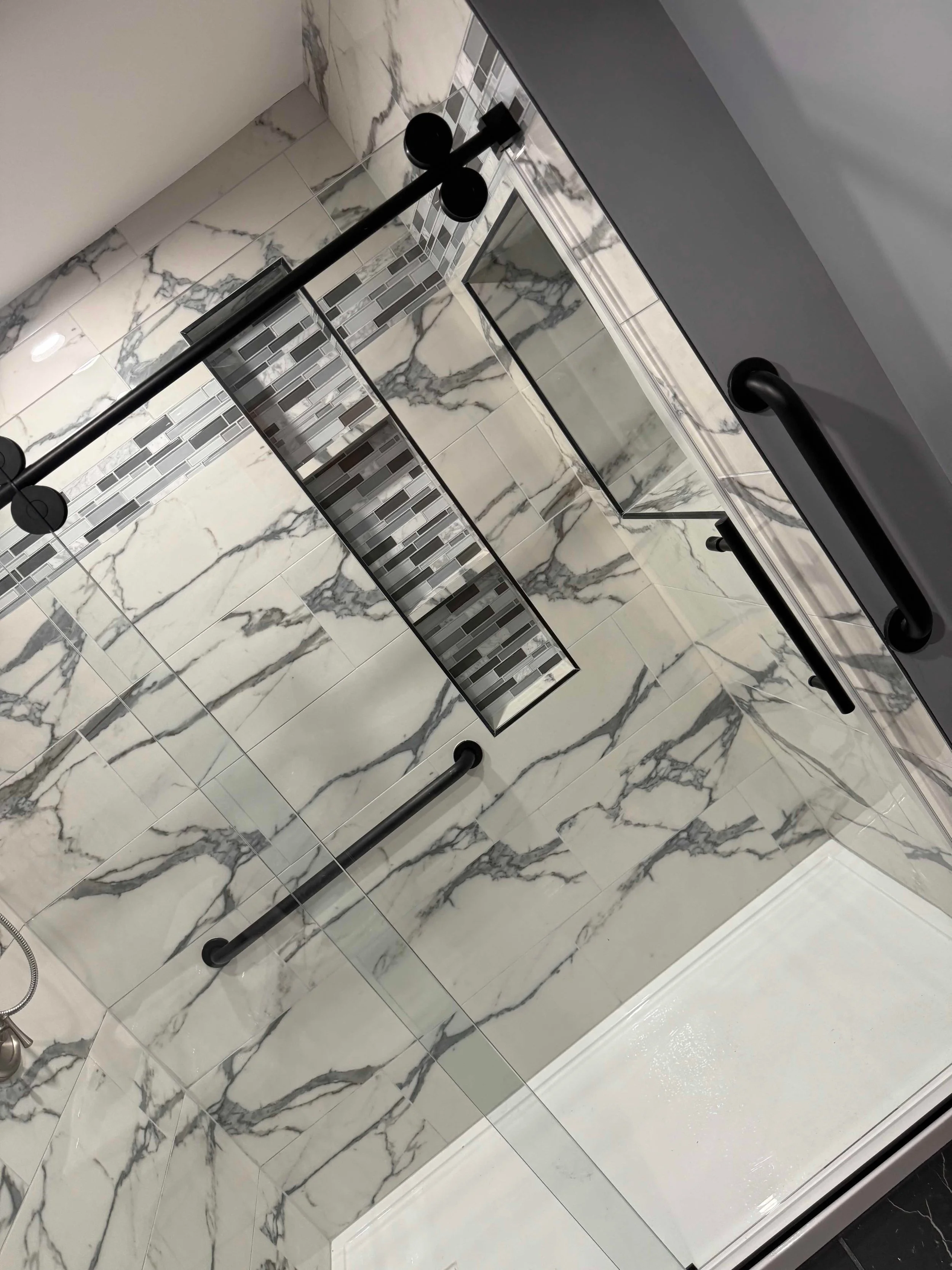 Shower with white marble tiles and black handrails.