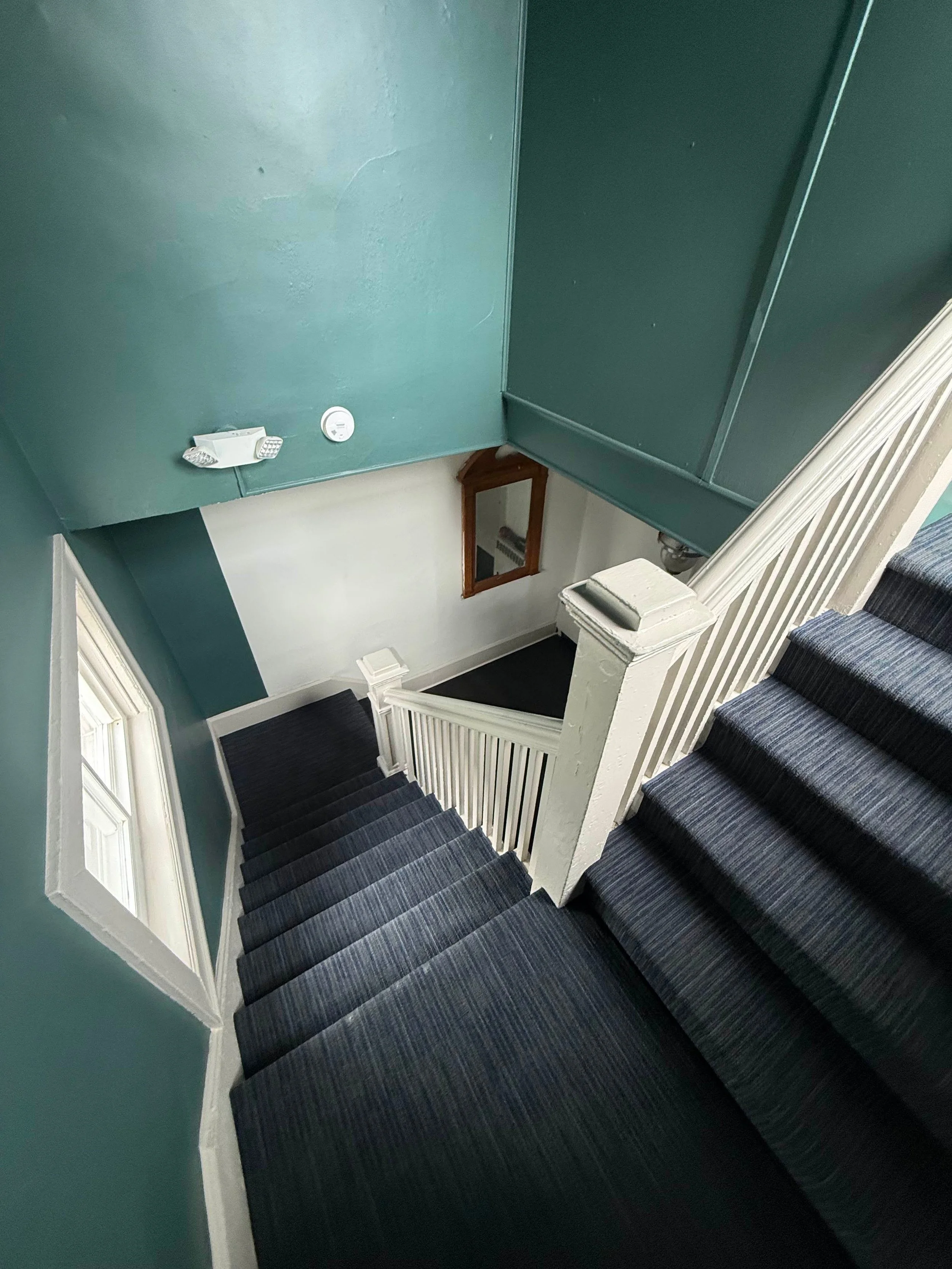 View of a staircase with striped dark gray carpet, beige walls, a mirror, and window panes at the top of the stairs.