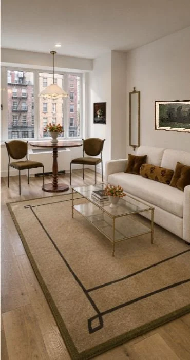 Living room with a white sofa, brown pillows, glass coffee table, beige area rug, and a dining area with a table, two chairs, and a window with city buildings outside.