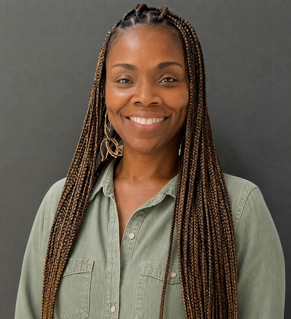 A young woman with long braided hair, wearing a green shirt and gold earrings, smiling against a dark gray background.