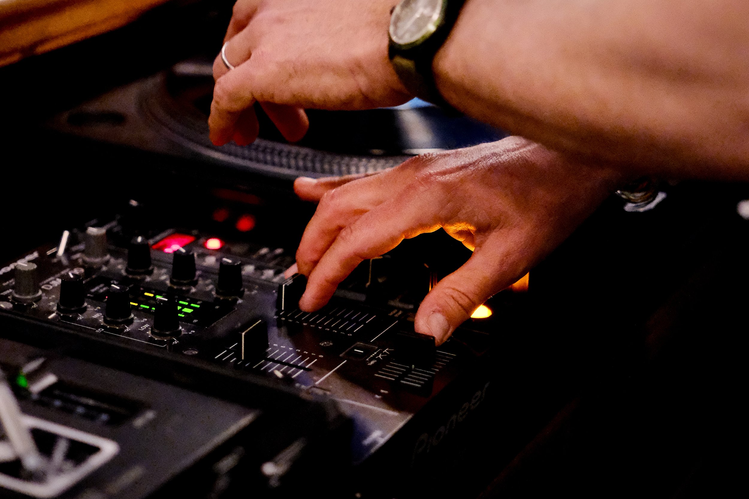 Close-up of a person's hand adjusting knobs on a DJ mixing console in a dimly lit environment.