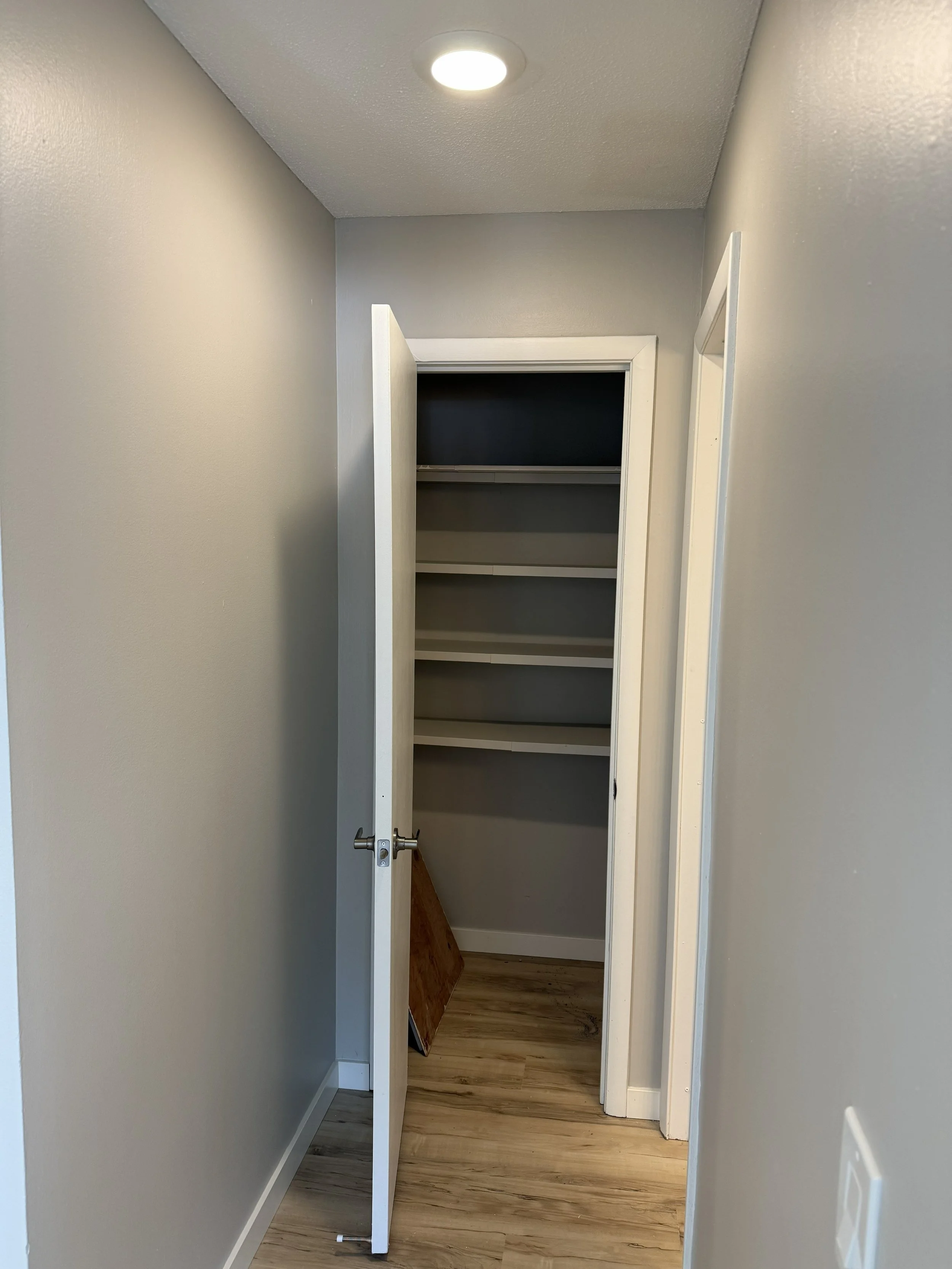 Small closet with white shelves inside, open door, and wood flooring.