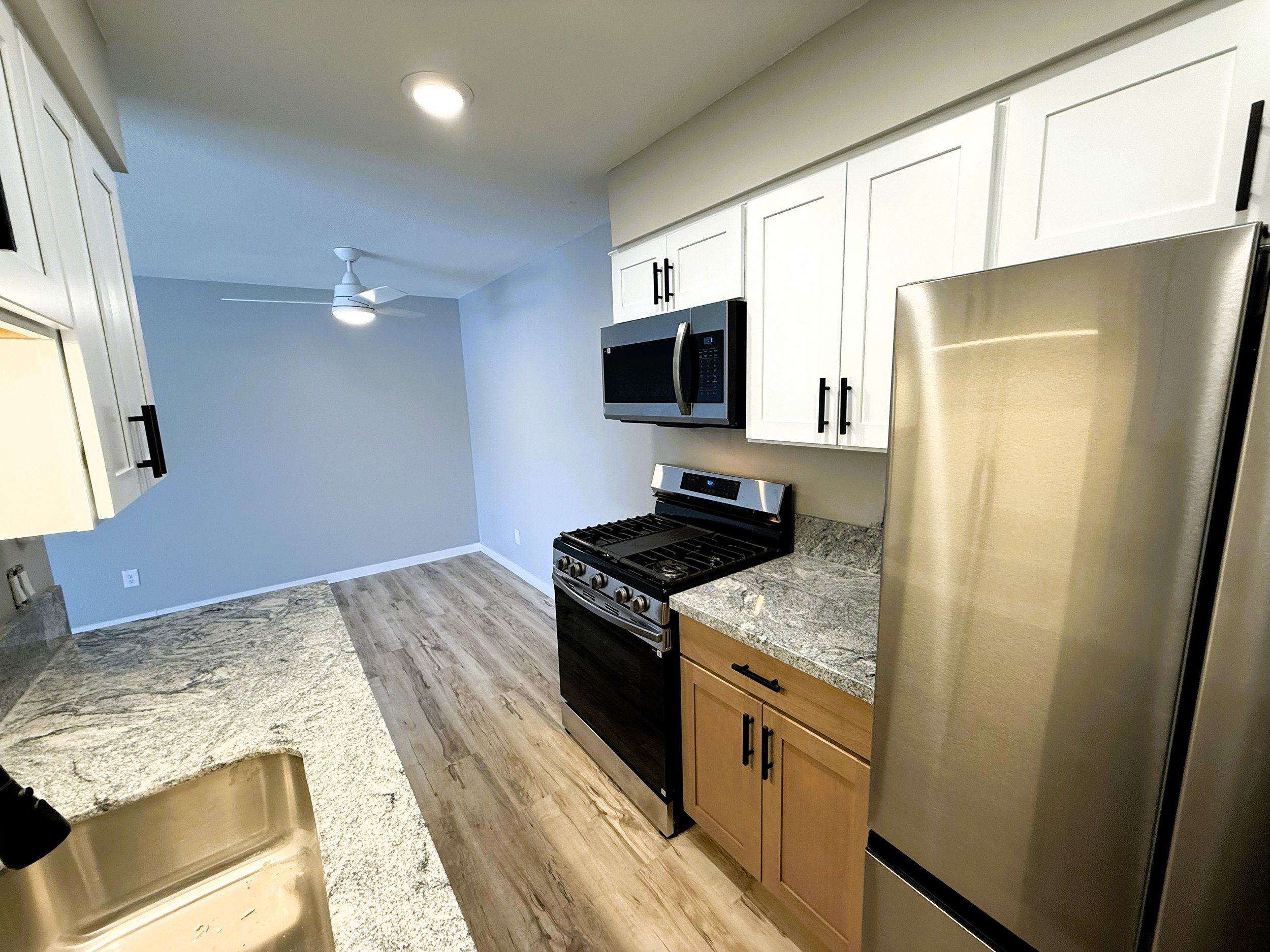 Kitchen with white cabinets, stainless steel stove and microwave, granite countertops, and wood-look flooring.
