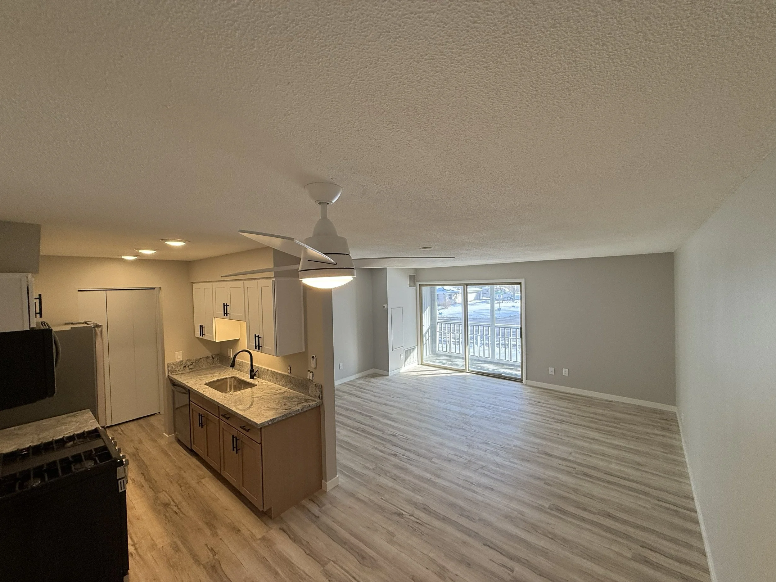 Open-concept kitchen and living room with sliding glass doors leading outside, ceiling fan, and hardwood floors.