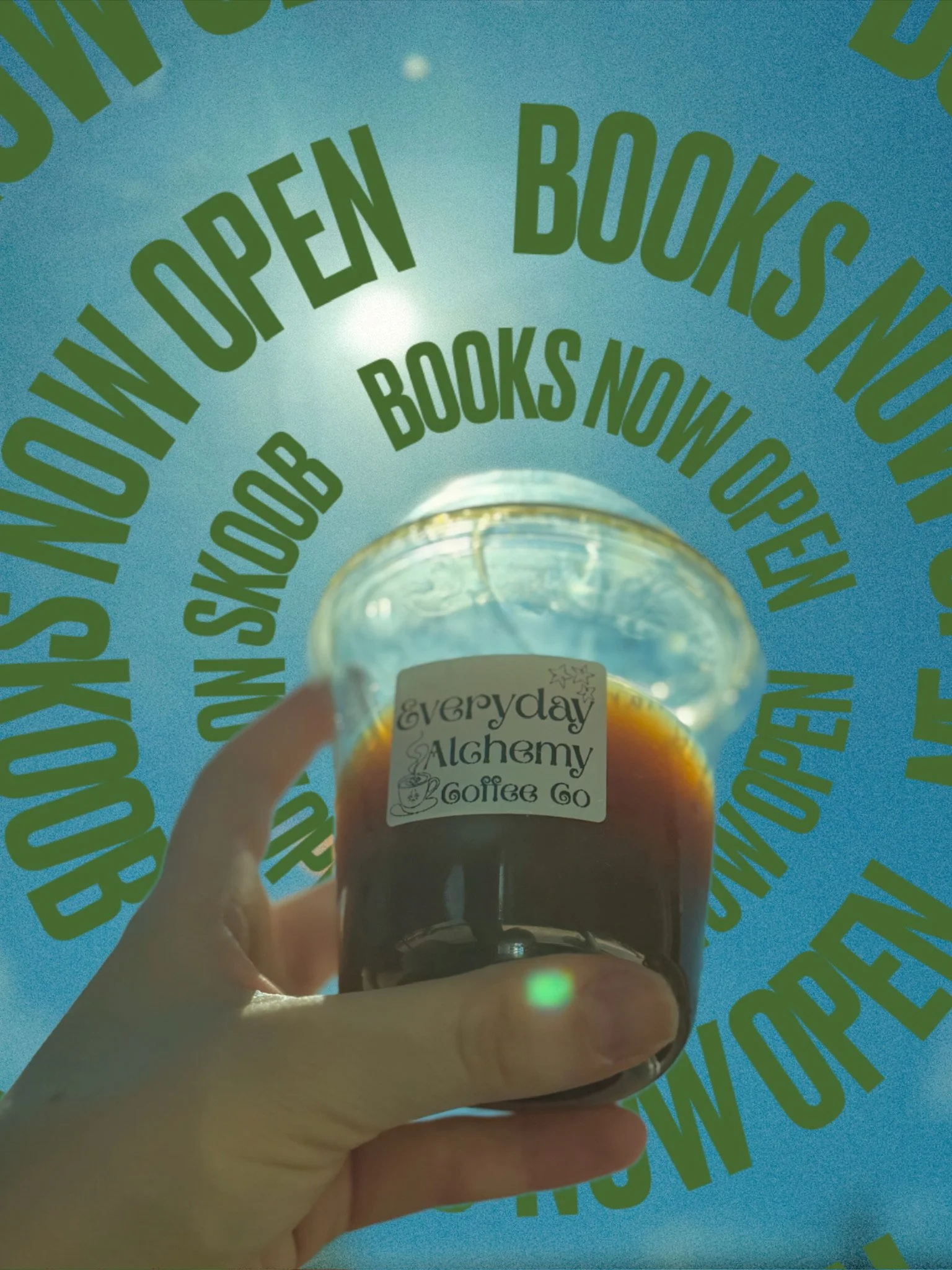 A person's hand holding a small plastic cup labeled Everyday Alchemy Coffee against a blue background.