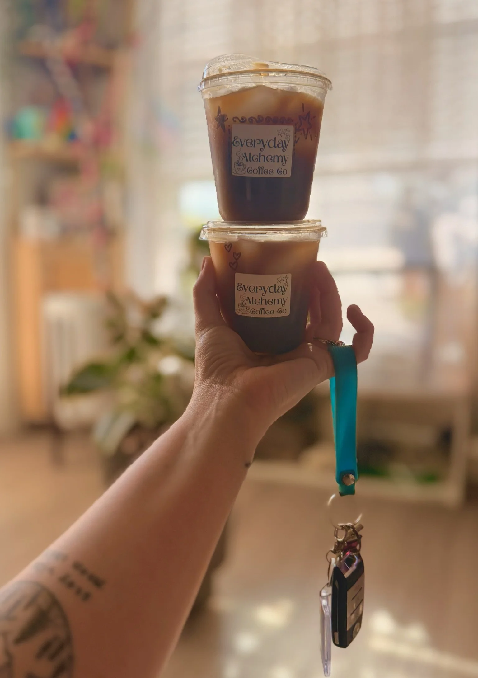 A hand holding two stacked Everyday Alchemy iced coffee cups.