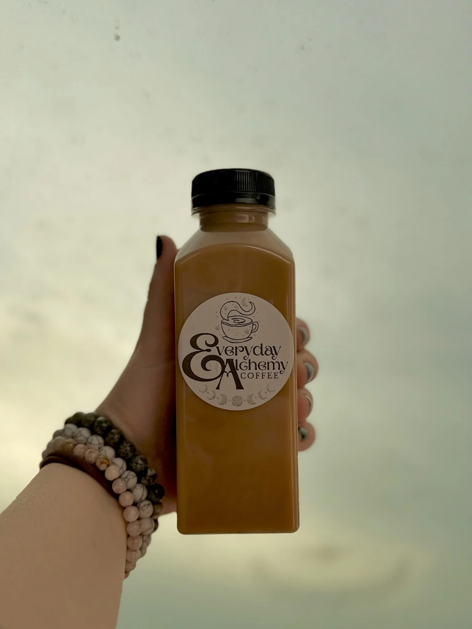 A hand holding an Everyday Alchemy Coffee bottled latte with the brand’s logo.