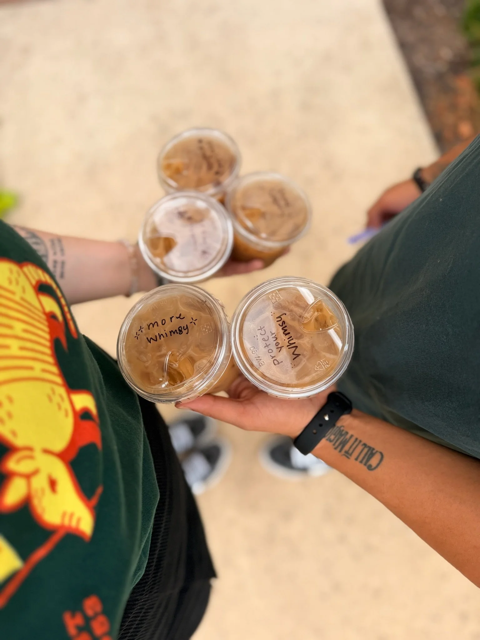 Two people holding five iced coffees with handwritten flavor names on the lids.