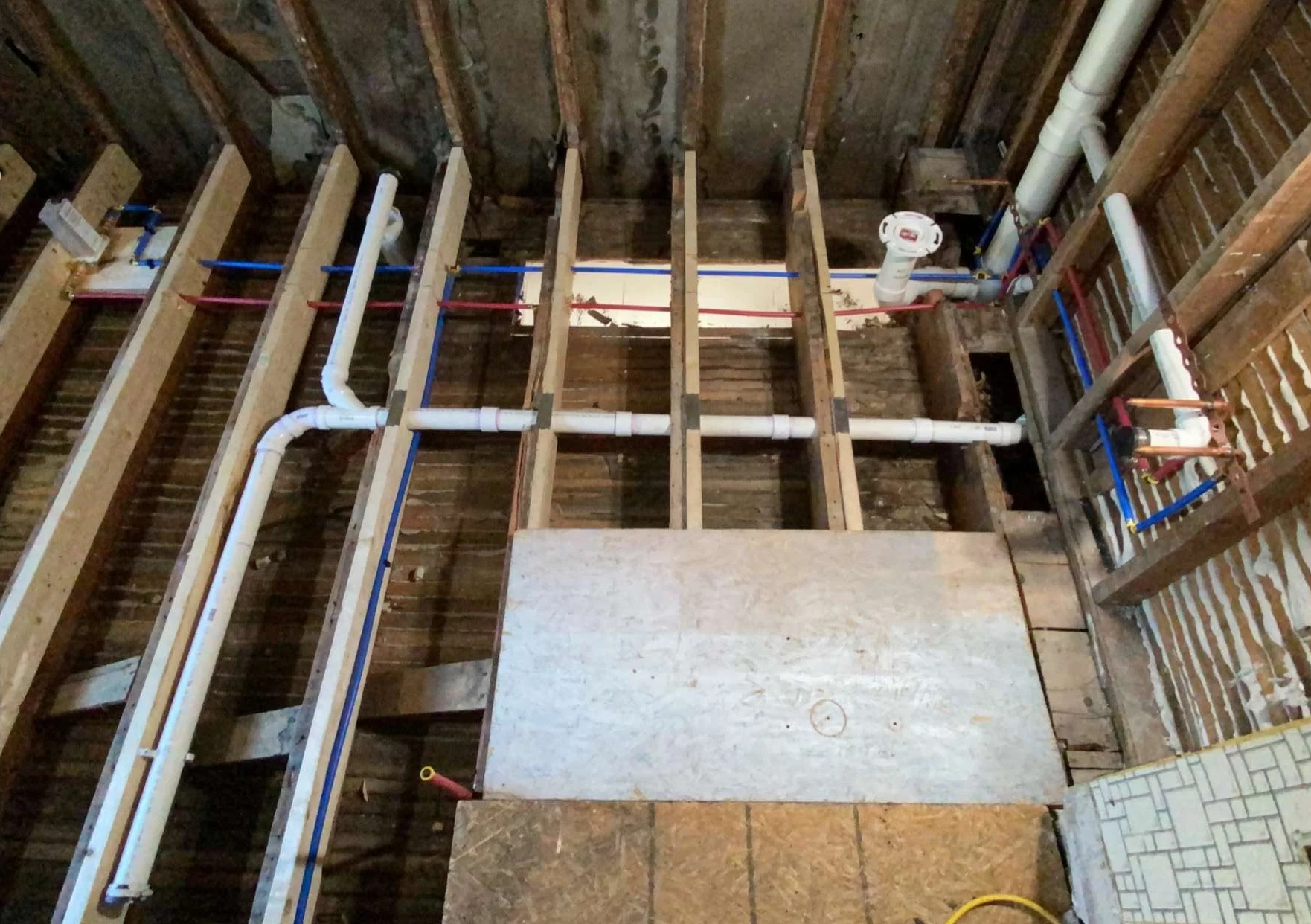 View of a construction site showing plumbing and framing for a wall, with exposed pipes, wooden studs, and unfinished wall sections.