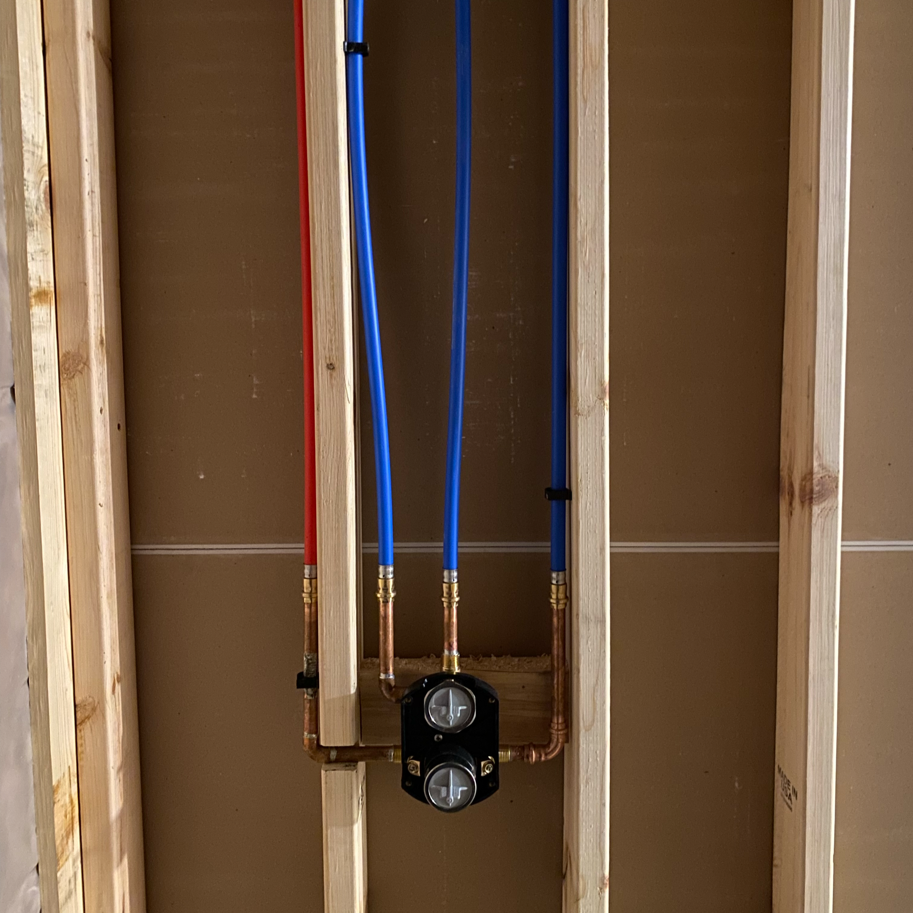Wood framing with plumbing pipes and a black valve valve mounted on a wall in a construction site.