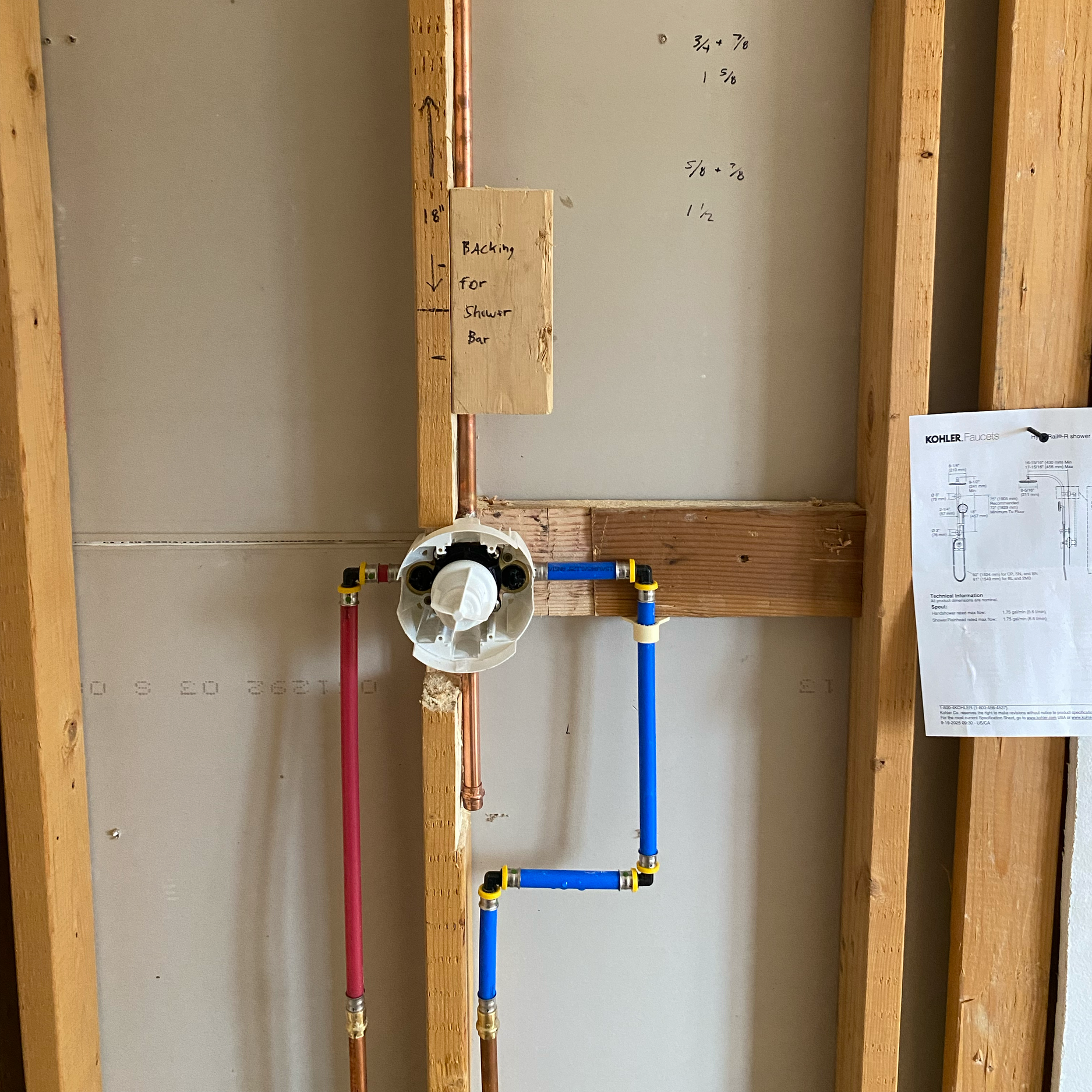 Wiring and plumbing pipes for a shower installation in a wall frame, with handwritten measurements and notes on the wall.