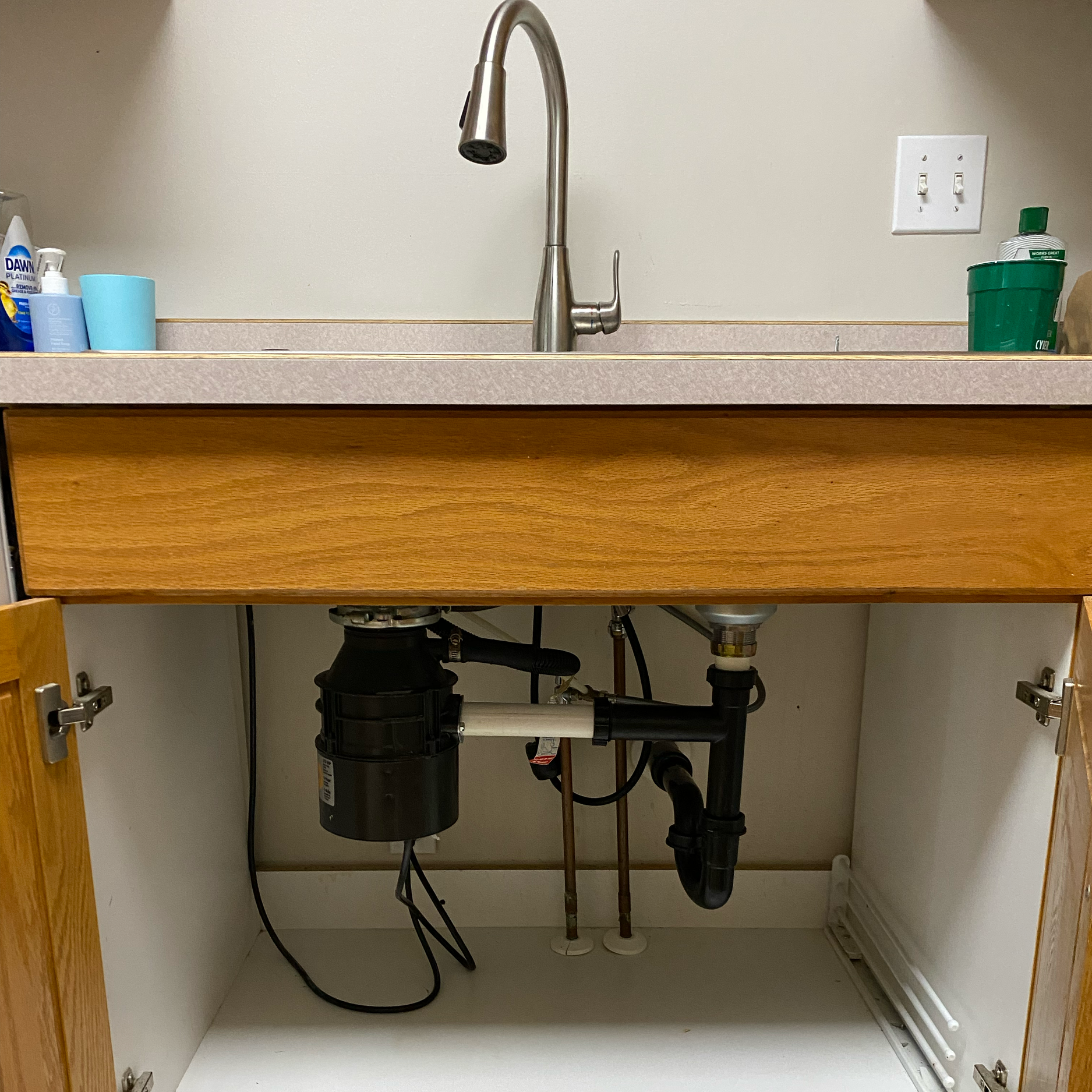 Undermount kitchen sink with a stainless steel faucet, soap dispenser, and cleaning supplies in a cabinet under the sink.