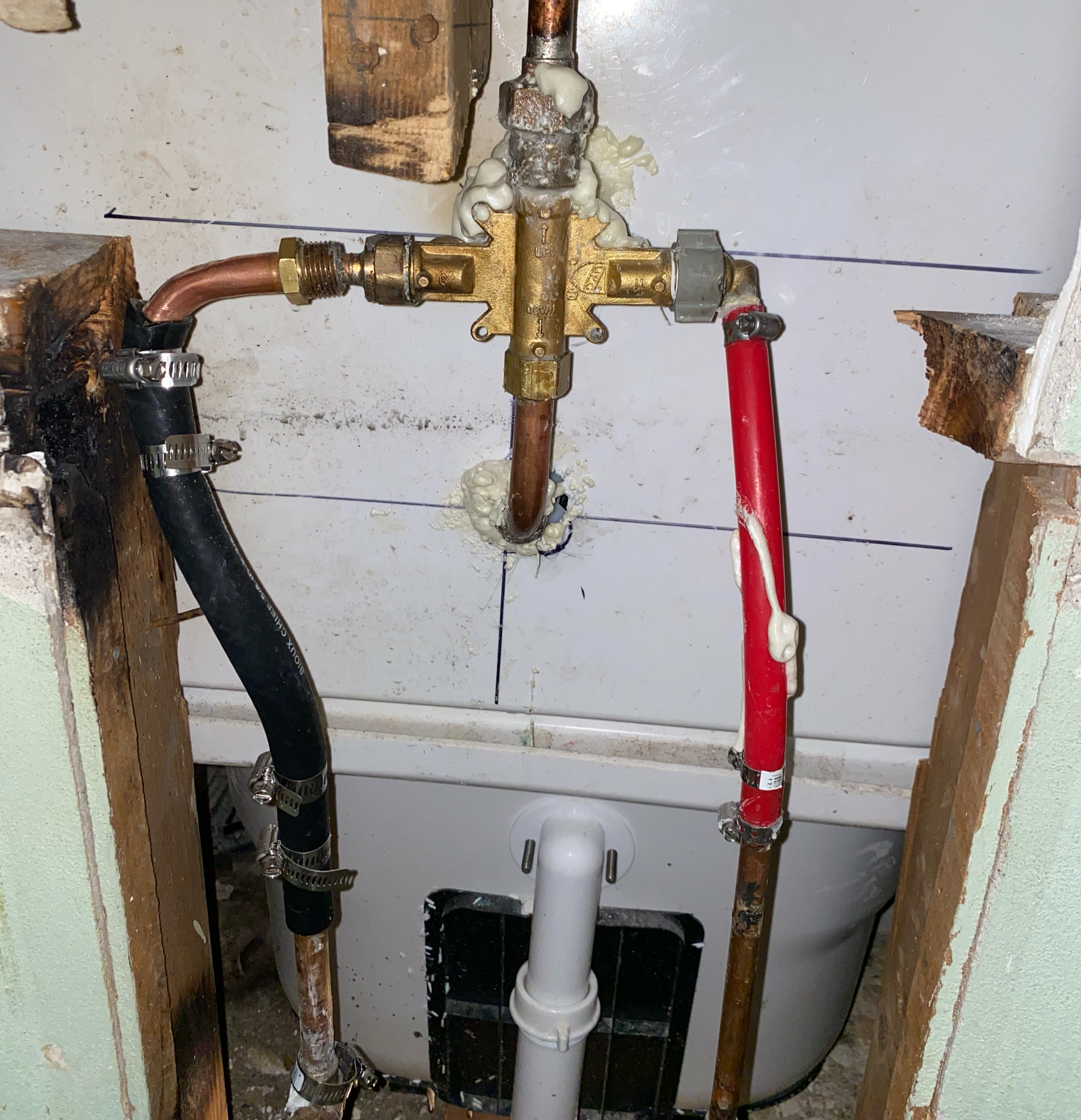 Plumbing setup with copper, plastic, and flexible pipes connected to a fixture in a wall cavity, with foam sealant around the connections.