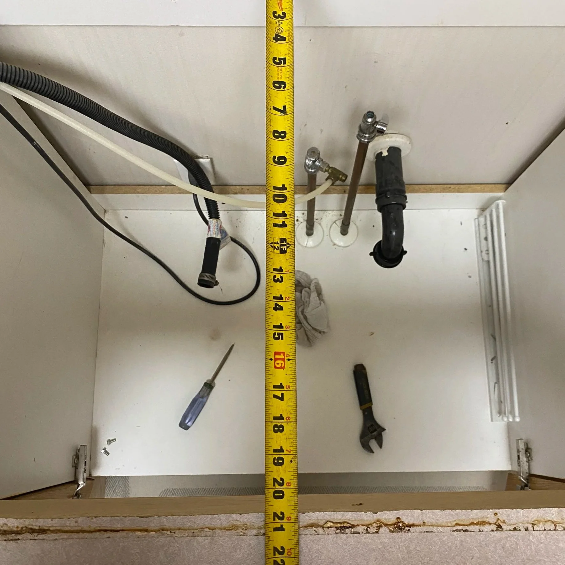 View of a utility wall with plumbing pipes, a wrench, and a screwdriver, with a measuring tape indicating height at approximately 17 inches.