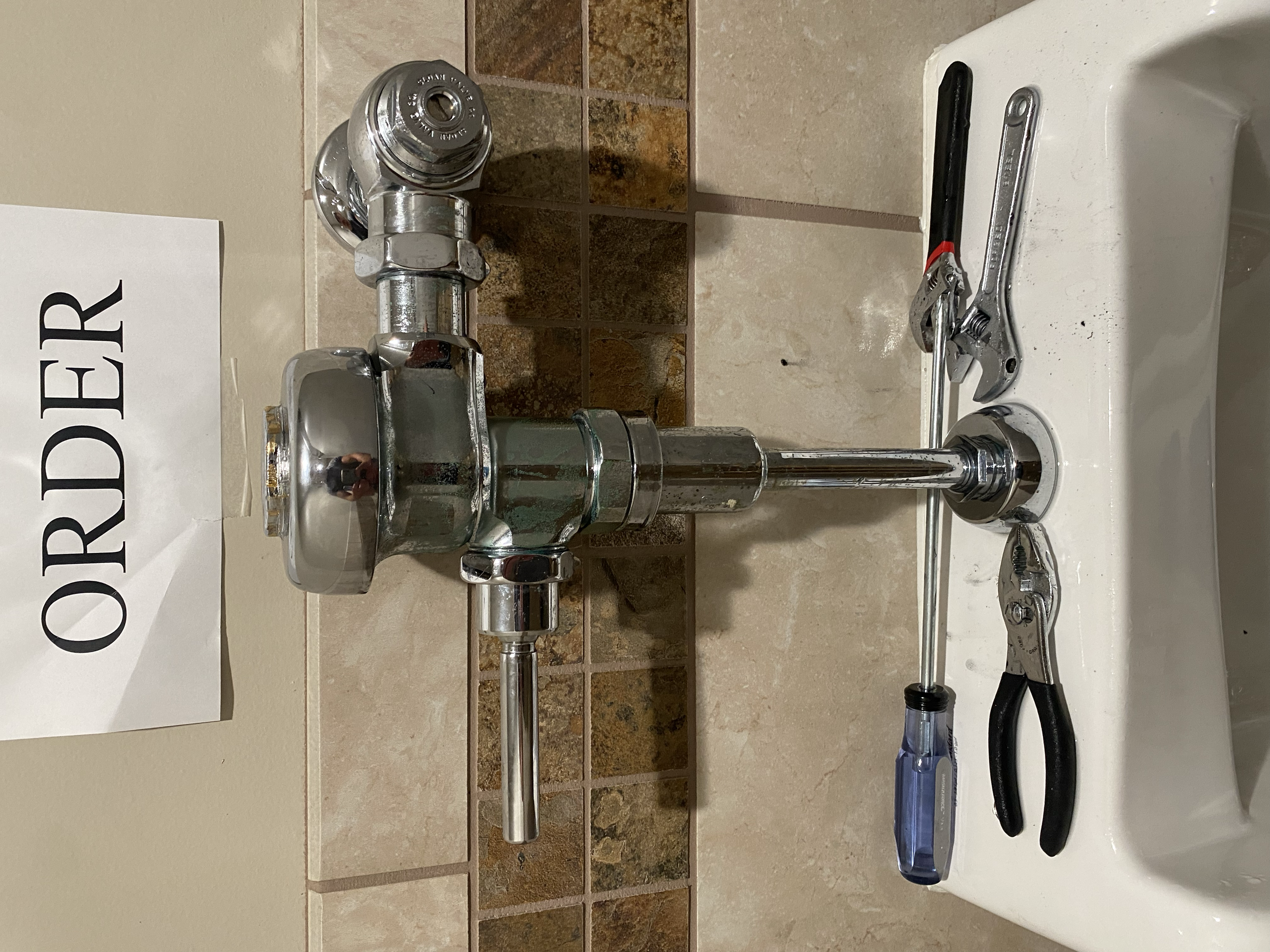 Disassembled chrome faucet and tools placed on a bathroom counter with a tiled backsplash.