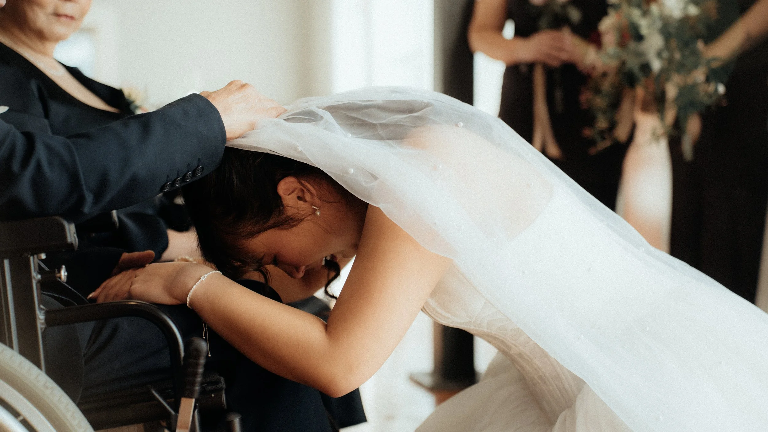 A bride leaning down to kiss a person in a wheelchair, during a wedding ceremony.