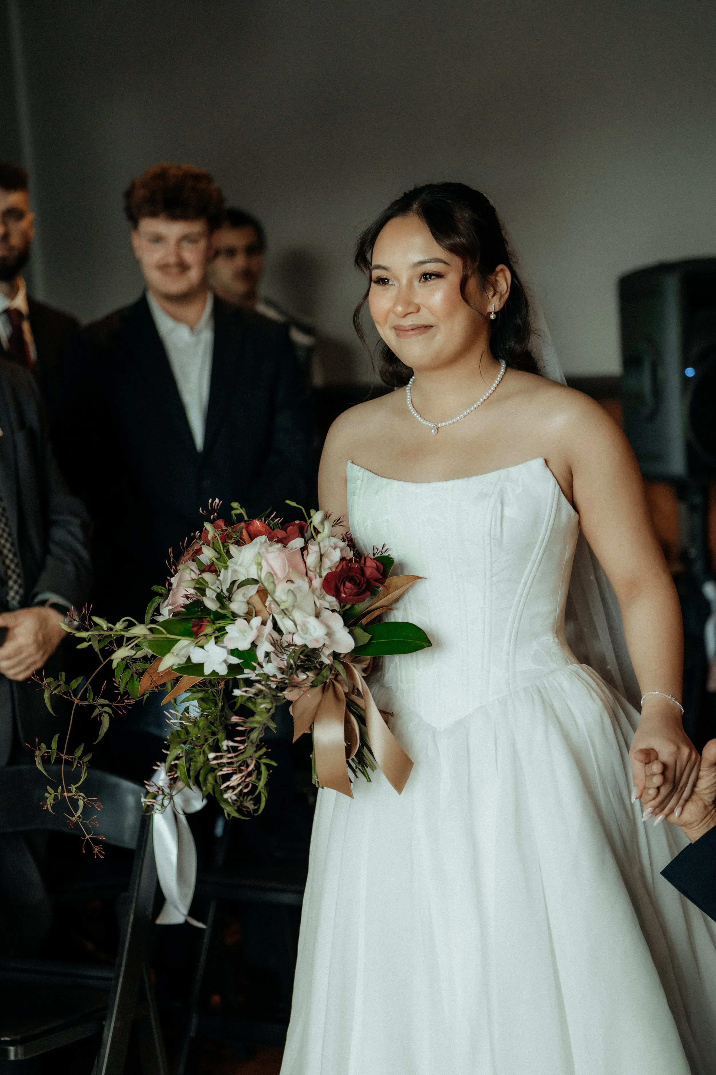 A woman in a wedding dress holding a bouquet of flowers during a wedding ceremony, surrounded by men in suits.