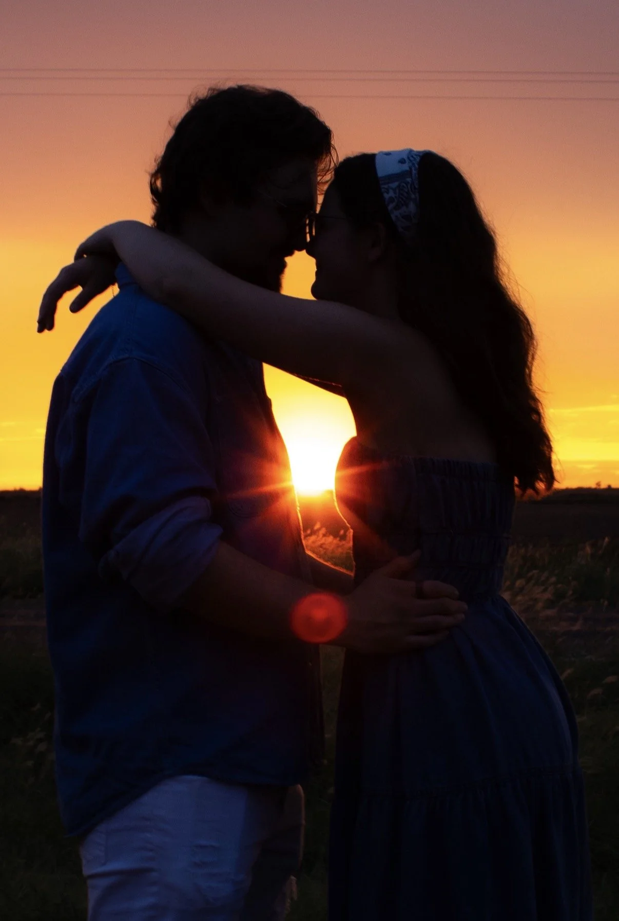 Silhouette of a couple embracing at sunset, with the sun setting behind them and a colorful sky in the background.