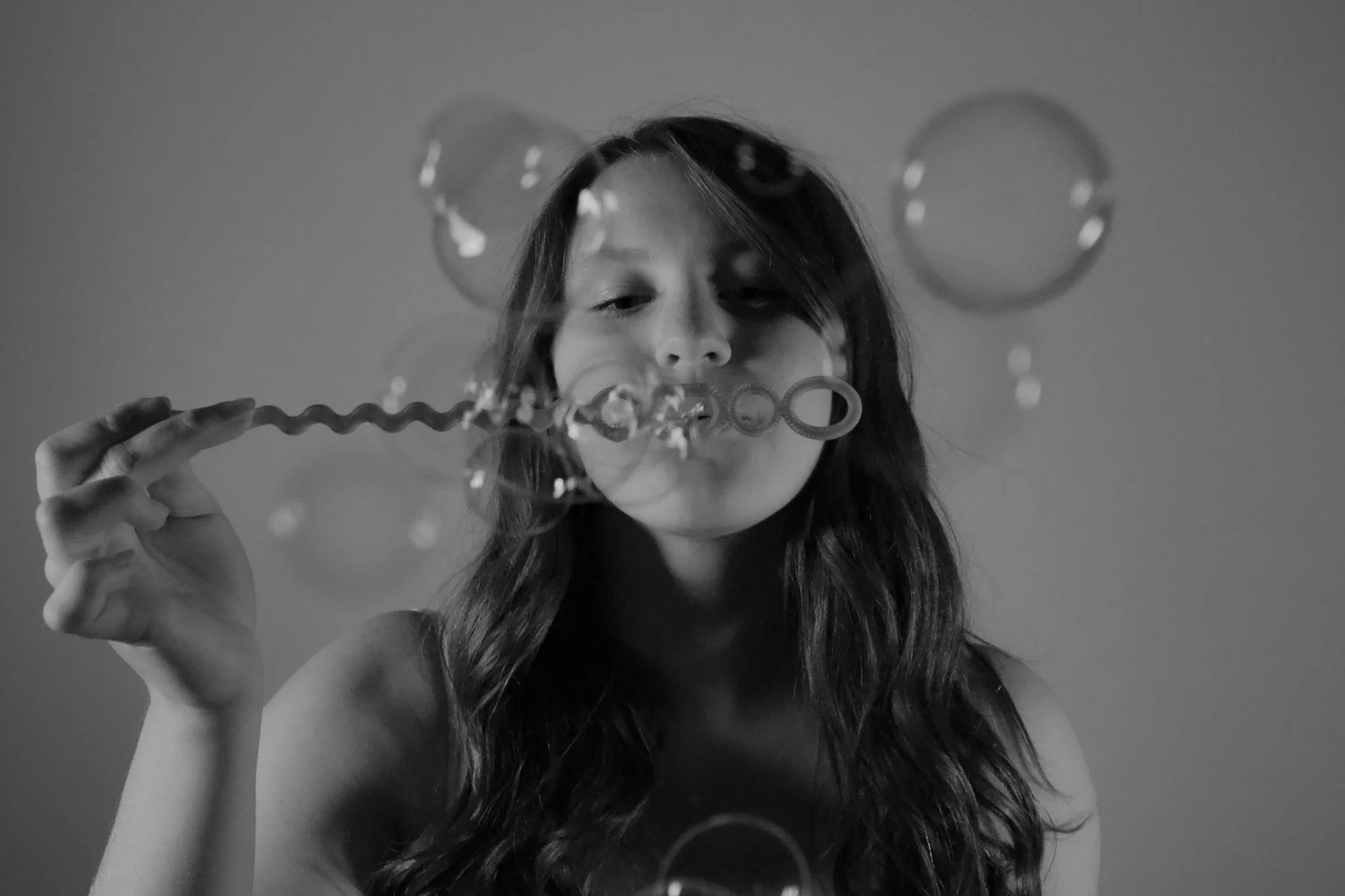 A young girl with long hair blowing bubbles using bubble wands, black and white photo.