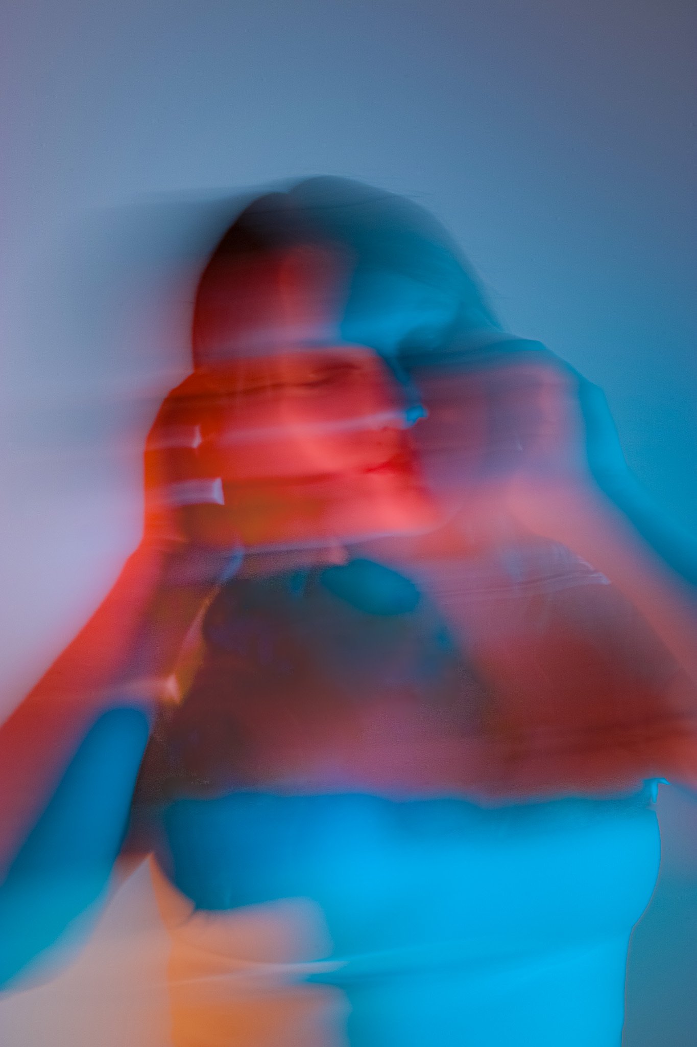 Blurry abstract photo showing a person in a red top, with their face and sign blurred, against a background with hues of blue, orange, and gray.