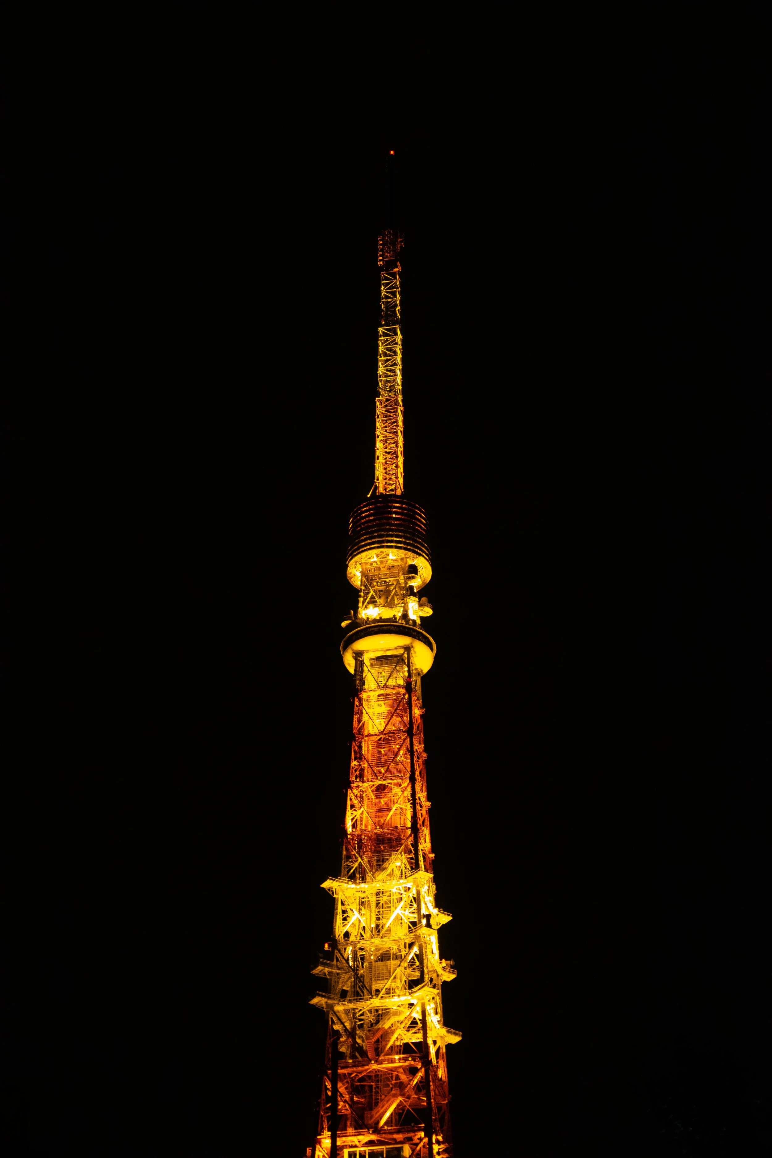 A tall communication tower illuminated in yellow lights against a dark night sky.