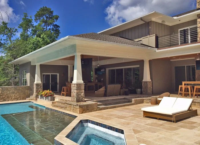 Luxury backyard with a swimming pool, stone patio, outdoor seating, and a covered patio area of a modern house with large windows and sliding doors.