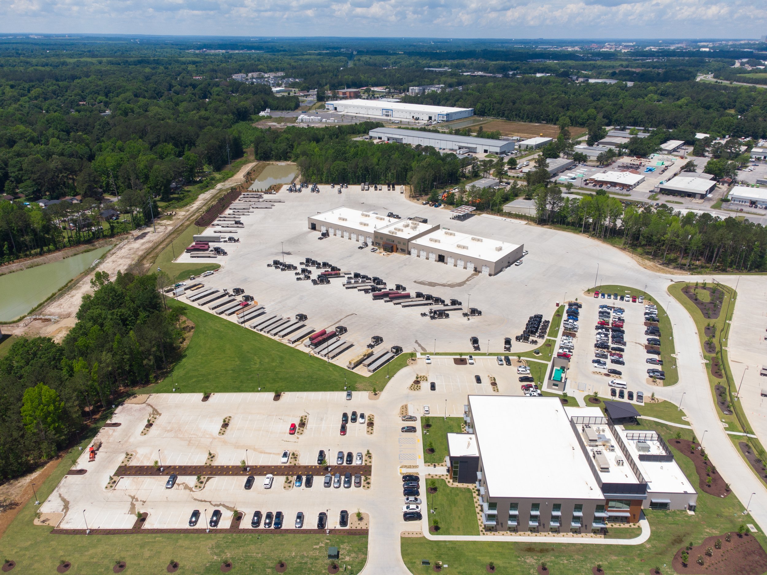 Aerial view of a large commercial area with parking lots, warehouses, and office buildings surrounded by trees and green spaces