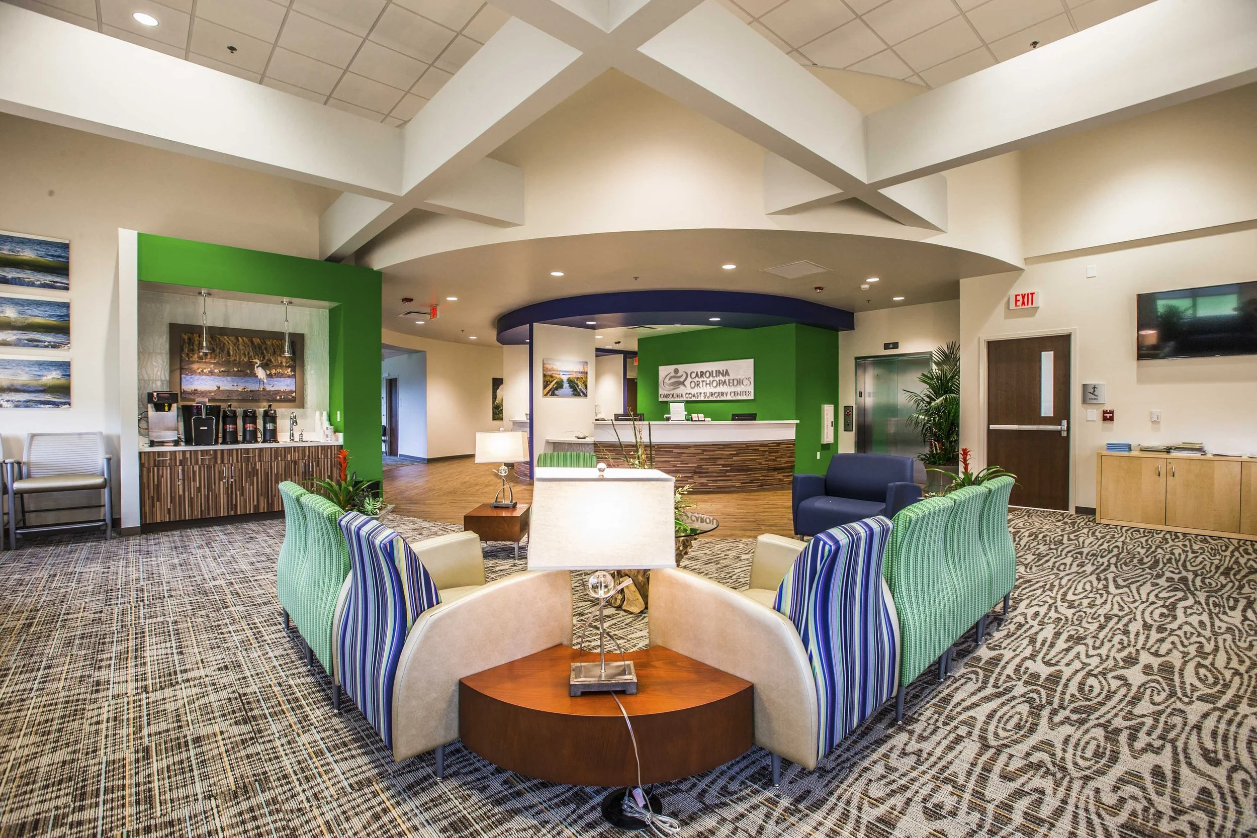 Indoor waiting area in a medical center lobby with a reception desk, seating chairs, and wall-mounted televisions.