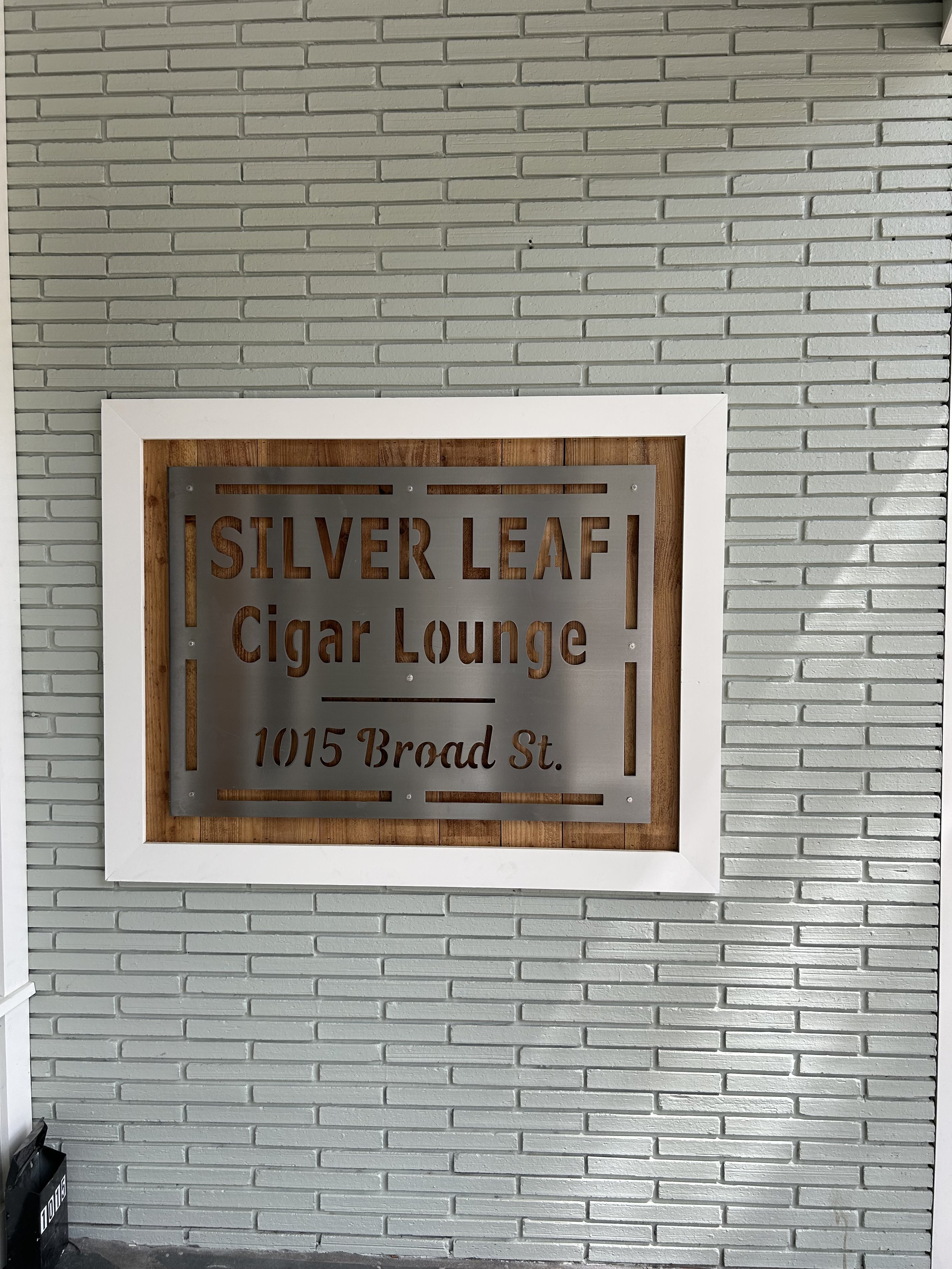 Sign on a wall that reads 'Silver Leaf Cigar Lounge 1015 Broad St.' with a brick wall background.