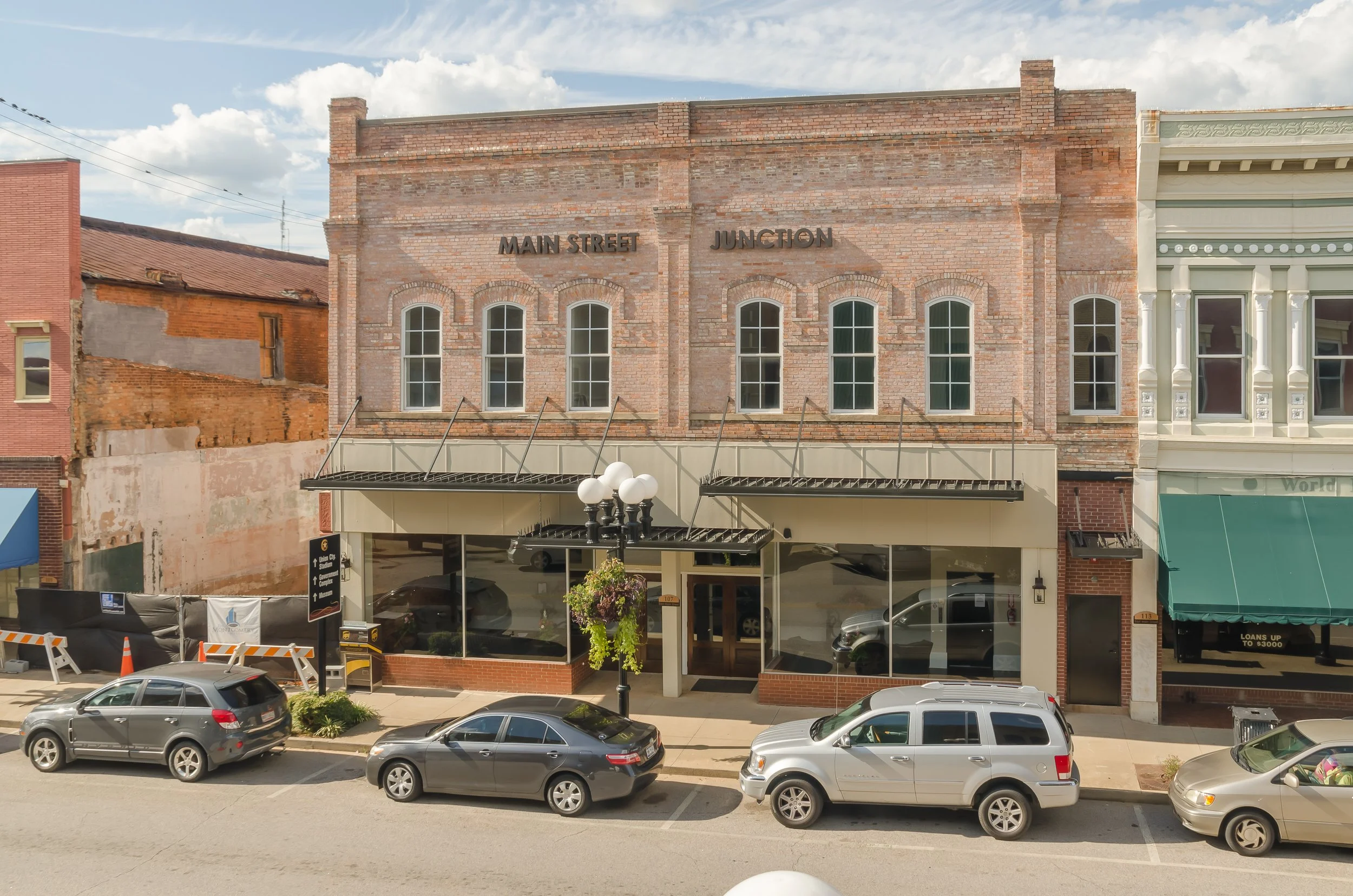 Street view of a brick building with signs reading 'Main Street' and 'Junction' at the top, with parked cars and a lamppost in front.