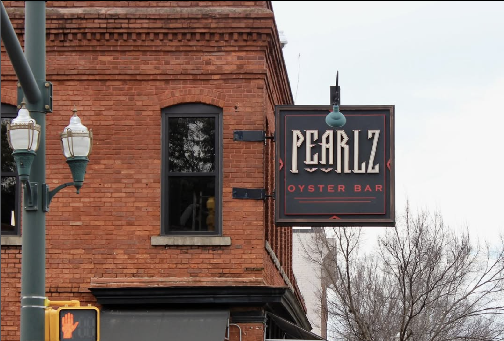 A sign for Pearlz Oyster Bar hanging outside a brick building under cloudy skies