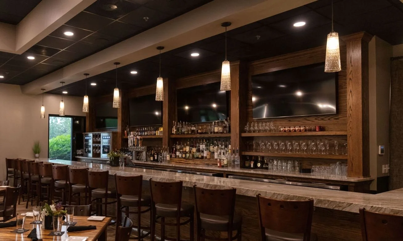 Interior of a bar with a marble countertop, wooden shelves stocked with bottles of alcohol, and hanging pendant lights.